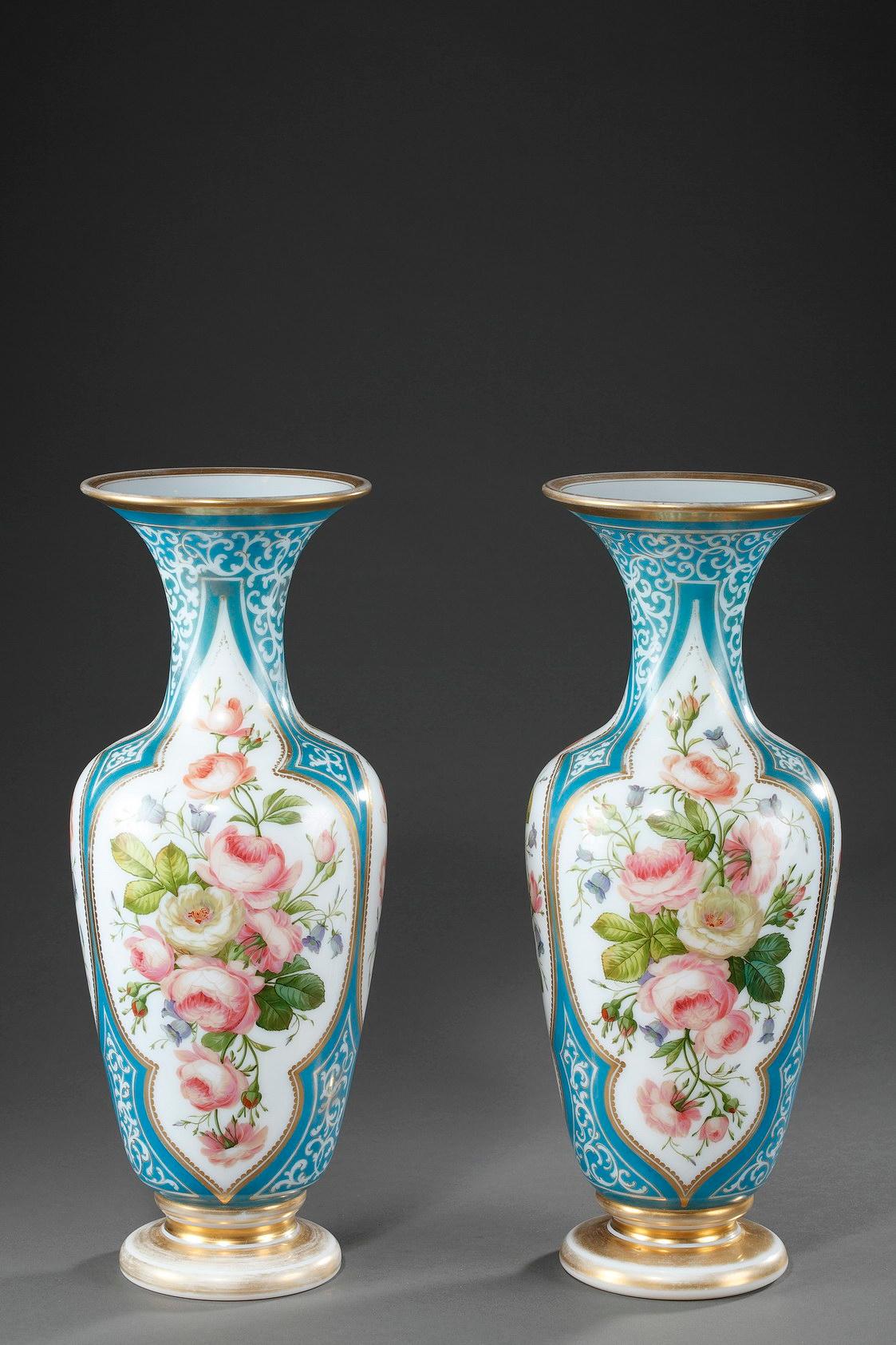 Coppia di vasi a forma di balaustro in smalto opalino decorati con fiori policromi in cartucce lobate su sfondo blu chiaro, accentuato da rinceau bianco e dorato. La base e il colletto sono sottolineati da strisce dorate. Leggera usura della
