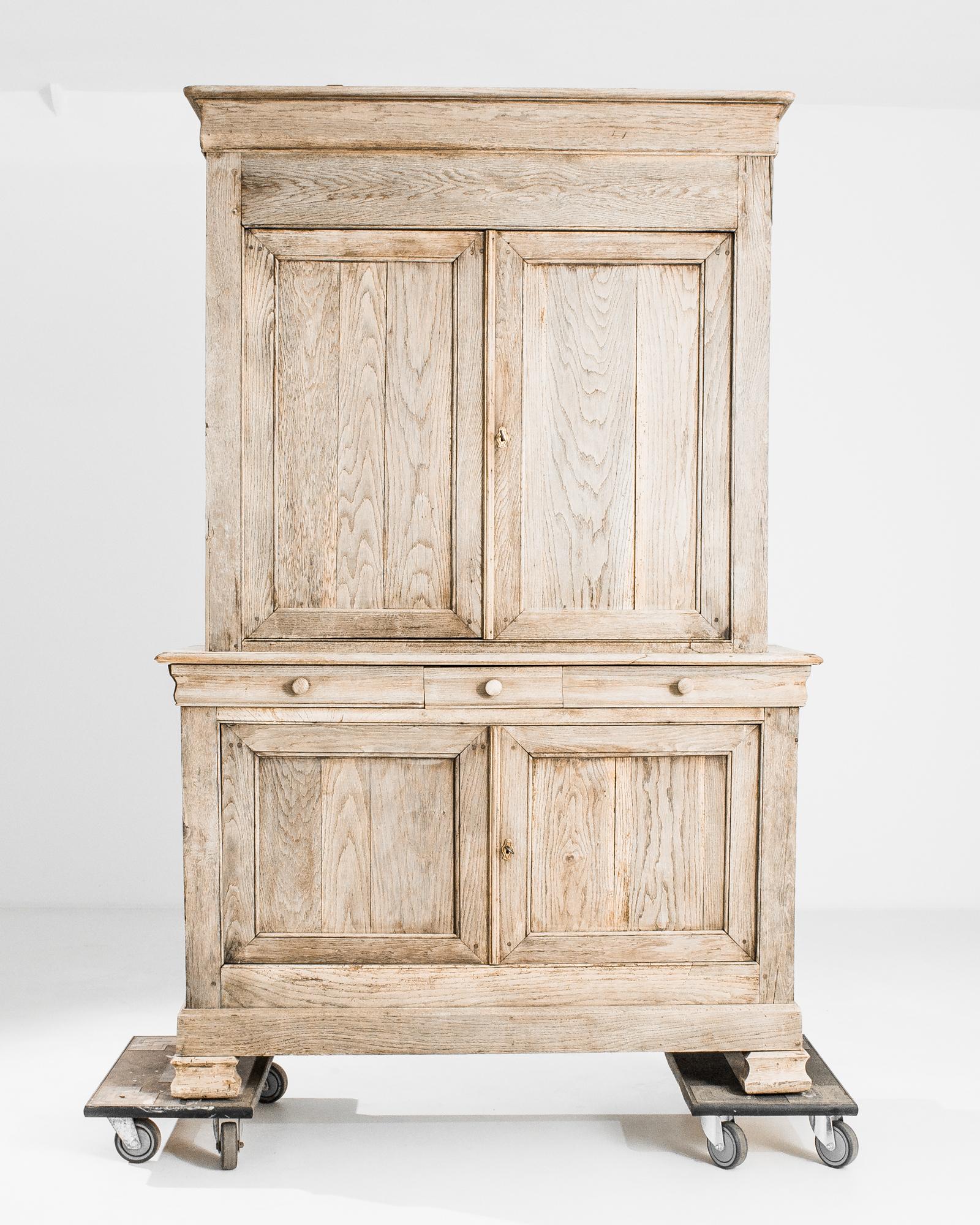 A bleached oak cabinet from France, produced circa 1880. A stately chest standing seven feet tall, this piece features an upper, locking, double door cabinet of three shelves, a lower double cabinet of two shelves, and a bifurcating row of three