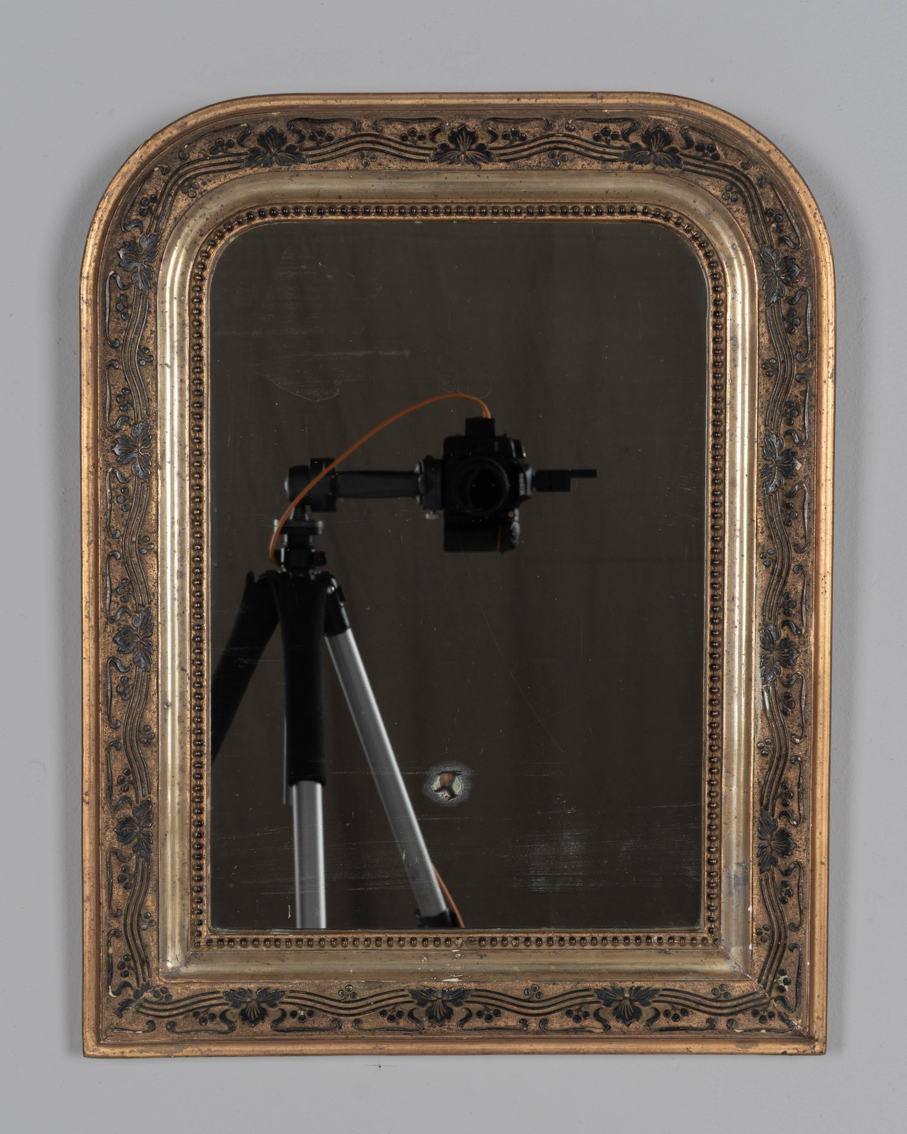 An early 20th century French Louis Philippe style mirror with curved top corners, black leaf vine pattern and inner bead border. In good condition with minor gilt loss. Original mirror has nice patina with a spot and with some light streaking.