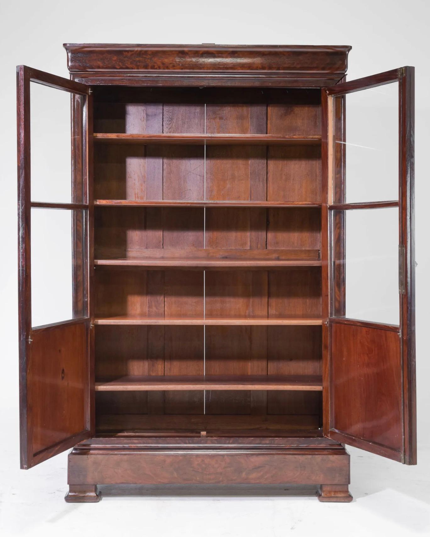 French Louis Philippe Style Mahogany Bookcase. Beautiful condition with patina - two doors with hand carved mahogany details framing two original panes of glass opening to a cabinet that is perfect for books, storage, or as a bar cabinet. 