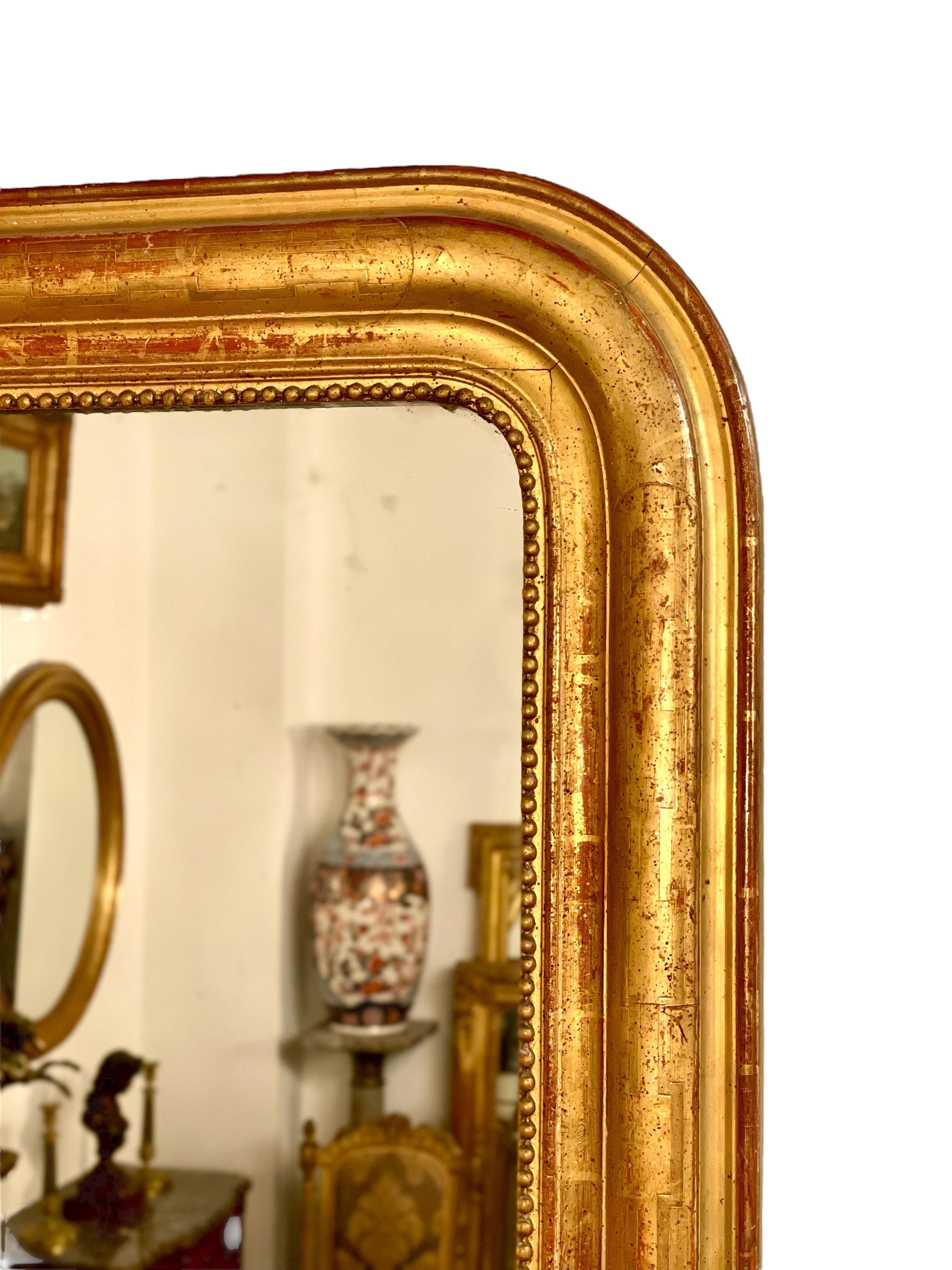 A handsome large Louis Philippe gilt wall mirror featuring the curved upper corners typical of the period, and a lovely moulded surround with an etched geometric design showing through burnished gold-leaf. A delicate string-of-pearls motif encircles