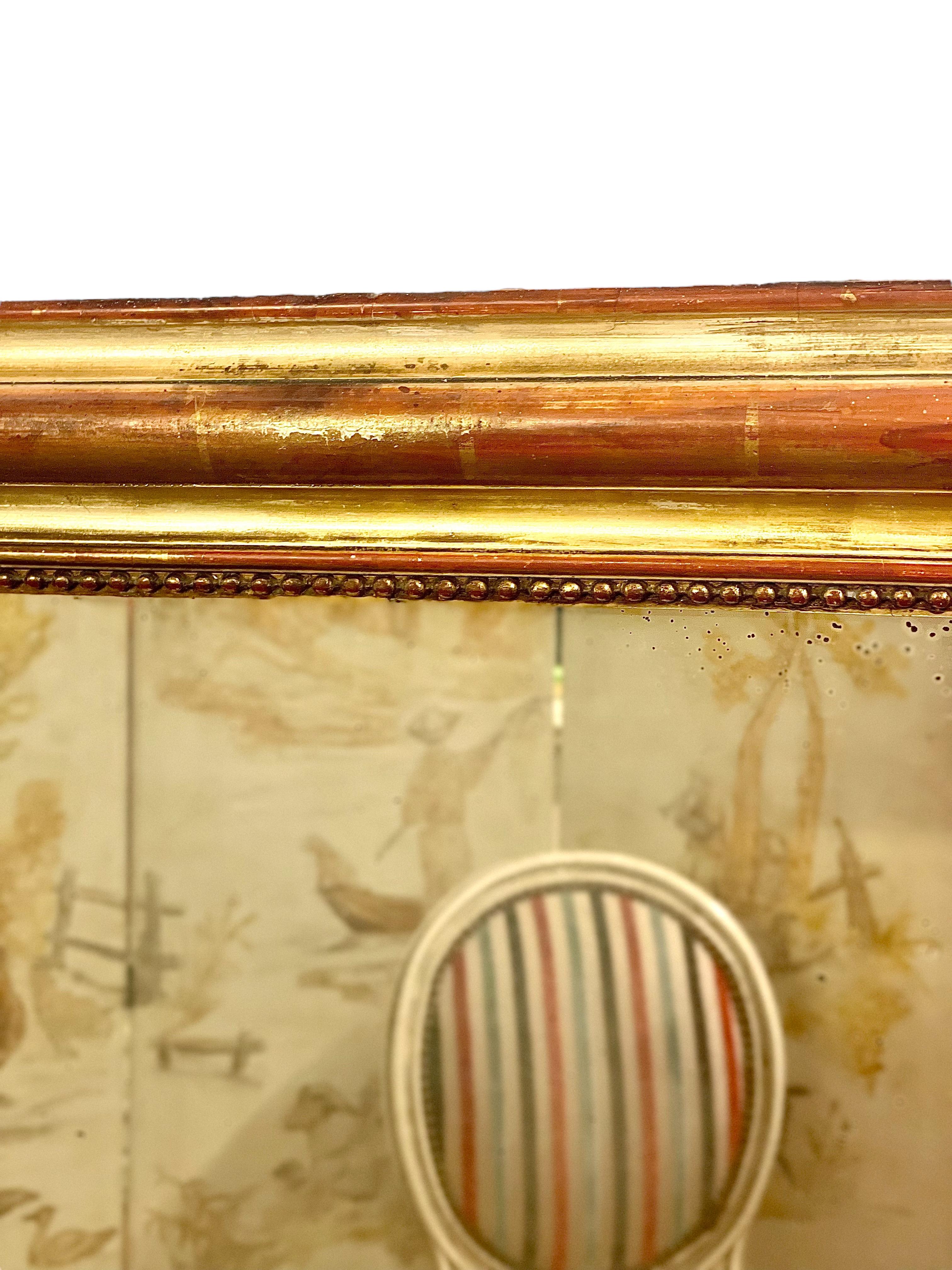 A fantastic French giltwood Louis Philippe period overmantle mirror, full of character and beautifully aged – the worn gilt of its undulating surfaces revealing the bold red wood underneath in places. 
The mirror has curved top corners, typical of