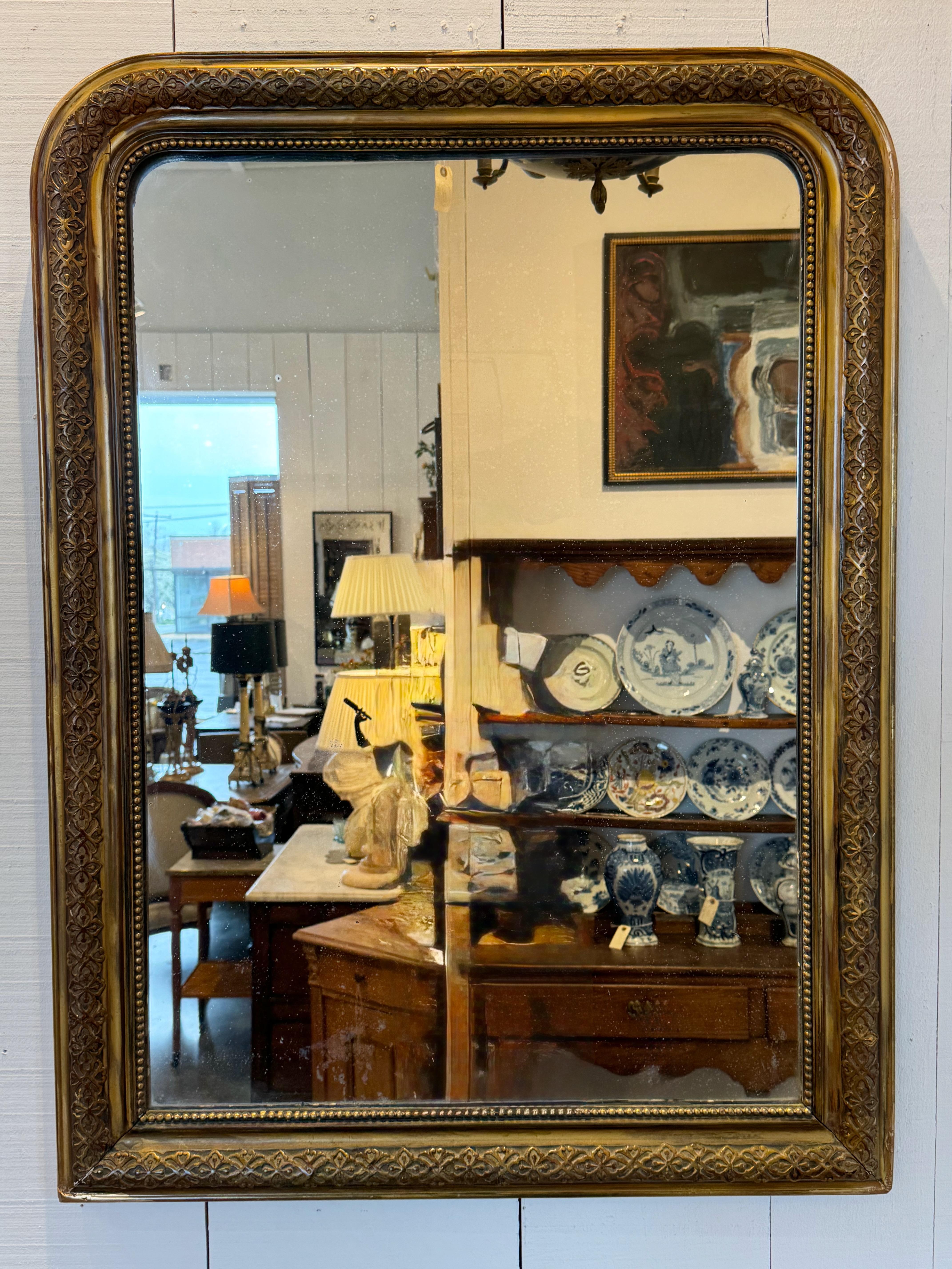 Mid-19th century Louis Philippe style mirror with a classic rounded rectangular form and giltwood frame. The surface features delicate foliate detailing and a subtle beaded inner border. Aged mirror glass adds depth and character. Timeless in