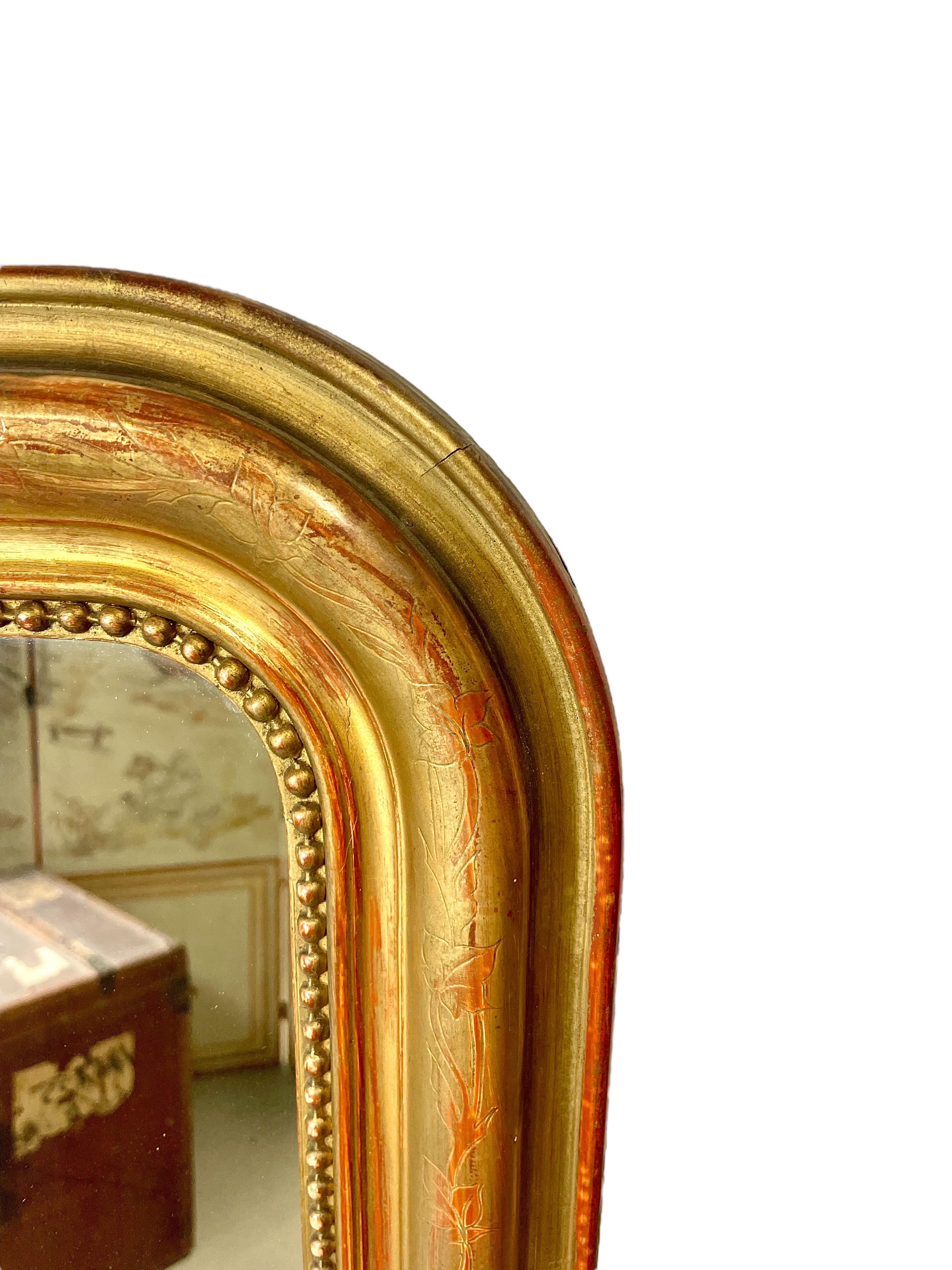 A charming Louis Philippe period gilt wood overmantle mirror, its burnished frame intricately etched with an intertwining design of ivy leaves and its inner rim edged with a classic 'string of pearls' motif. 
The original gilt finish of the frame is