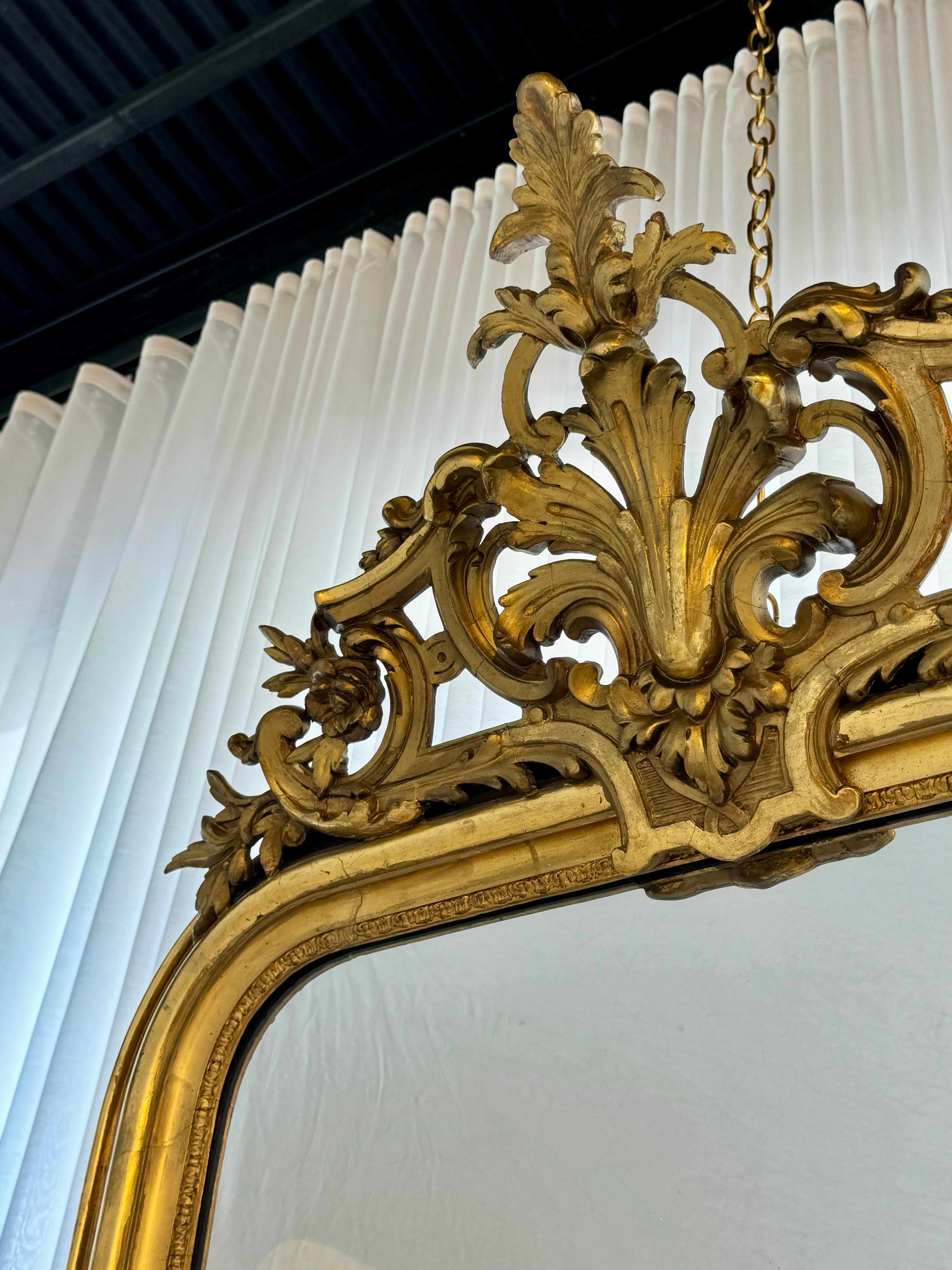 19th Century French Louis Philippe giltwood wall mirror, in an elegant tall and slender form, having a molded and gilded frame with an acanthus liner on the interior. The striking upper pierced cartouche pediment at the crown reaches shoulder to