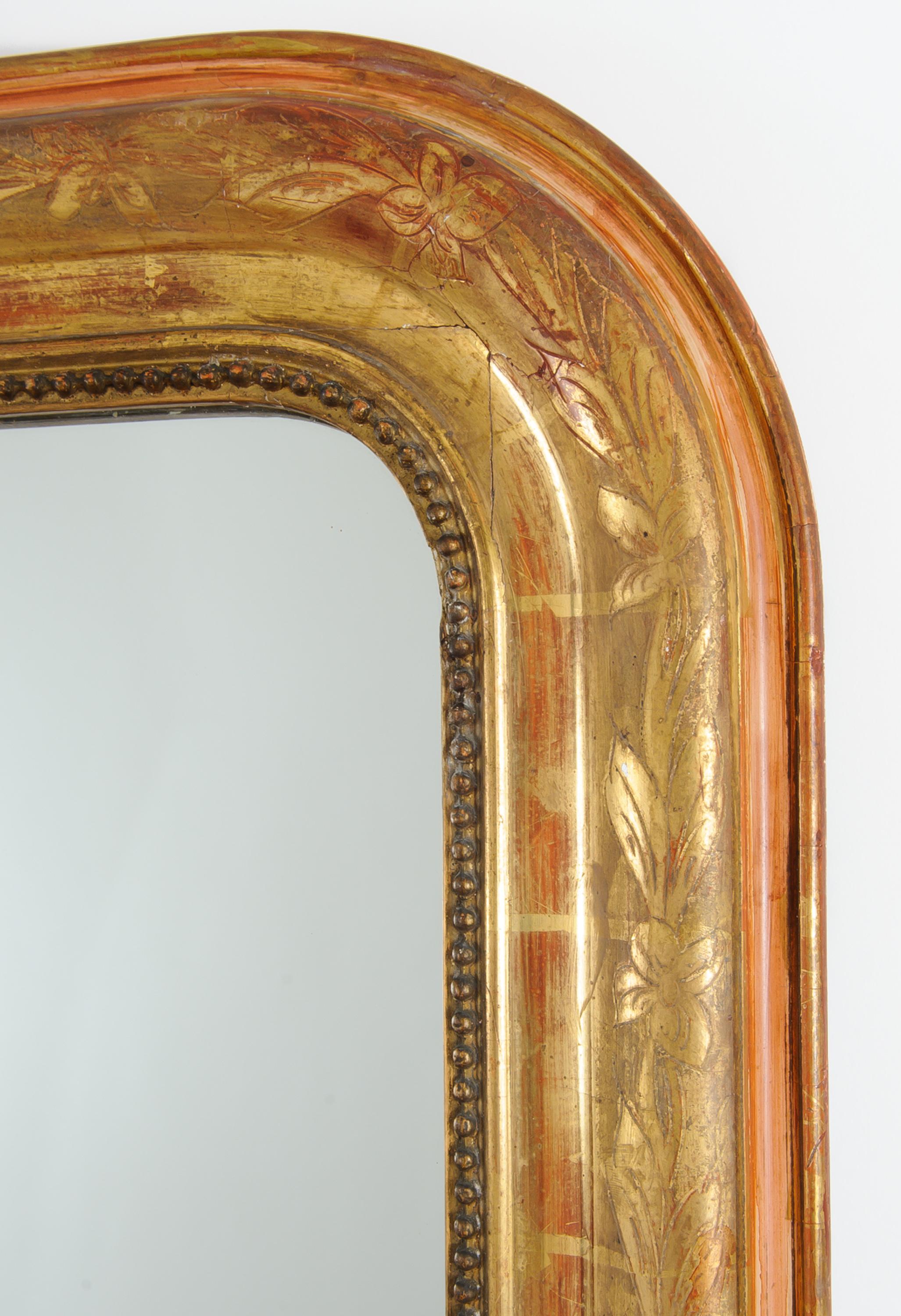 This period mirror has the original bright gold leaf finish with a floral motif on the full frame.  It has a finely carved bead detail surround. Red bole layer is apparent and adds a lovely complement to the gold leaf finish, which has a bright tone