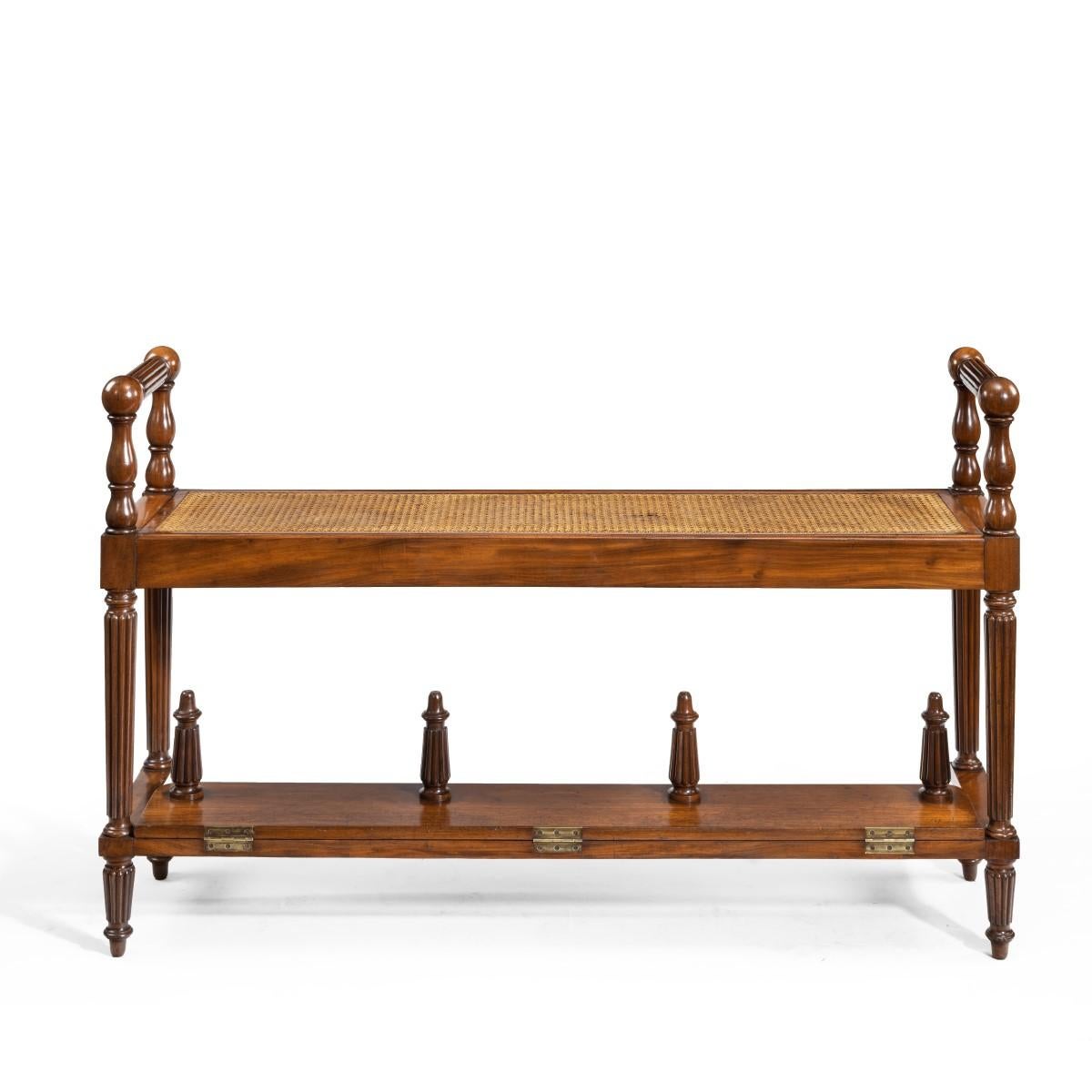 An unusual Louis Philippe mahogany hall bench with a folding footrest, of narrow rectangular form with turned handles at either end set upon tapering reeded supports and feet, the hinged footrest with similar turned feet, French, circa