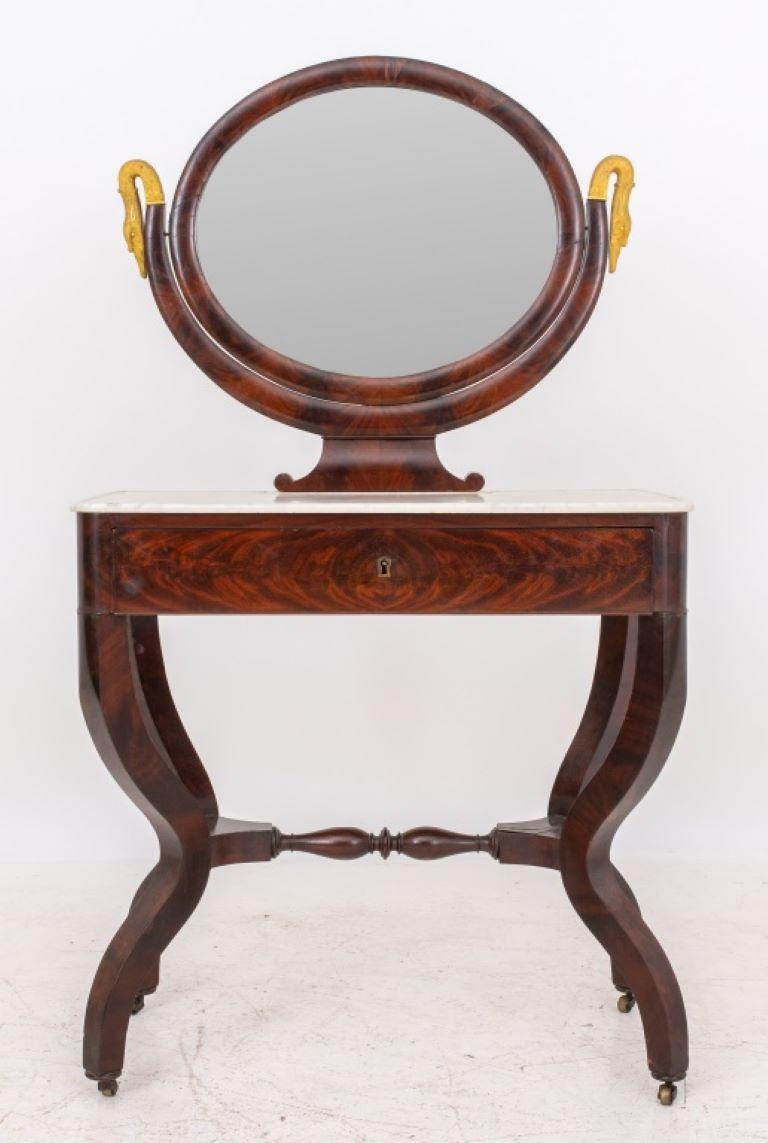 Louis Philippe flame mahogany veneered vanity table with marble top, circa 1840, the oval mirror within a parcel-gilded swan support on a rounded rectangular lipped white marble top over one long drawer with two curule supports connected by a turned