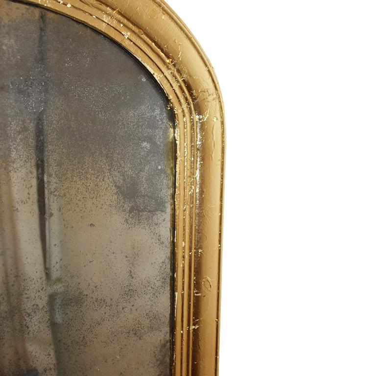 French Provincial giltwood Louis Philippe gold leaf mirror. A beautiful grand wood mirror with gold leaf detail. The bottom corners are slightly rounded with a traditional rounded top. The molding around features a banded wooden frame. The mirror is
