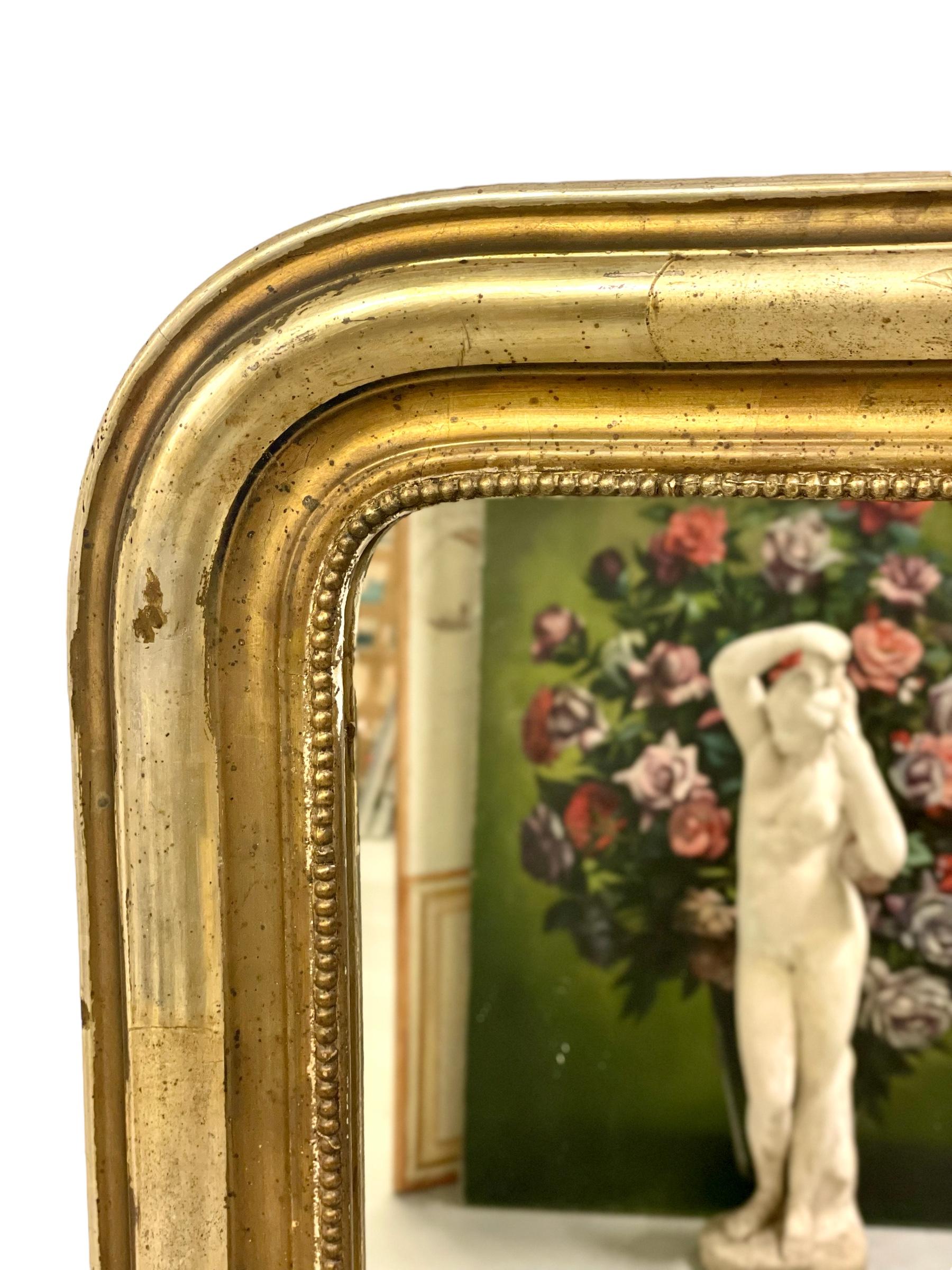 A gleaming Louis Philippe style gilt wood mirror, its burnished frame displaying the simple, clean lines and curved upper corners typical of the period. The original gilt finish of the carved and moulded outer frame is nicely worn, giving the mirror