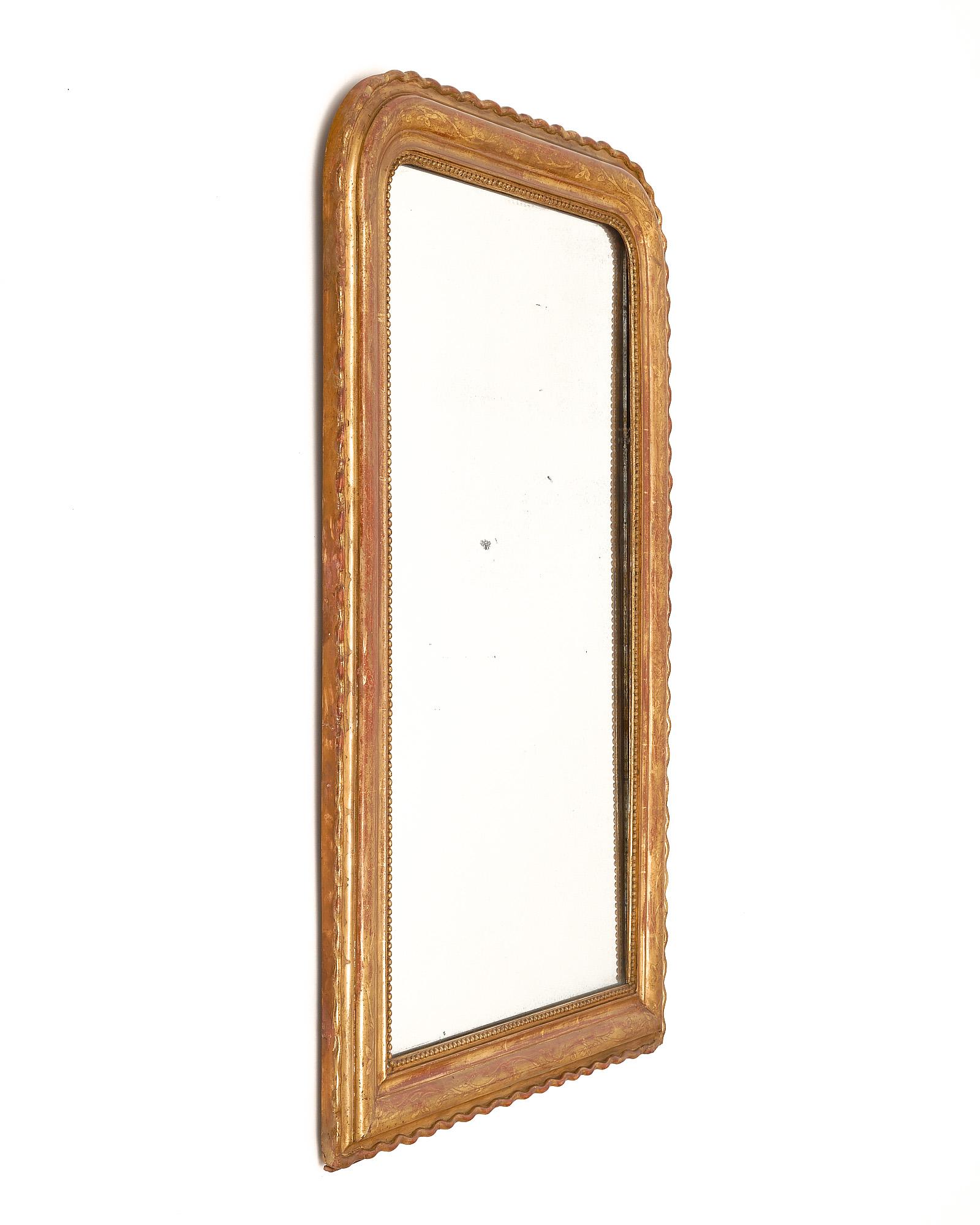 Miroir, français, d'époque Louis Philippe. Ce miroir est en bois massif, sculpté à la main et stuqué. Le miroir néoclassique présente des ciselures florales et la glaçure sienne est recouverte d'une feuille d'or 23 carats patinée. Nous avons été