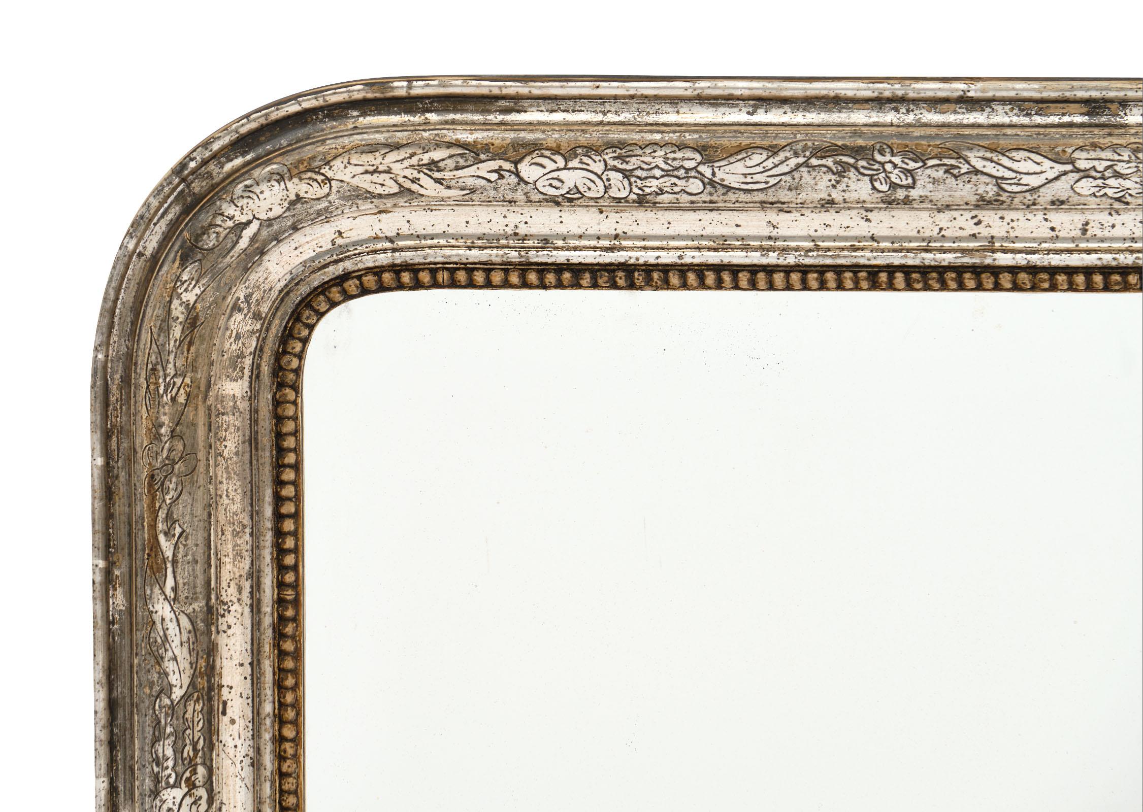 French silver leaf Louis Philippe period mirror with a beautiful engraved frame with floral motifs. We love the original patina and classic rounded corners.