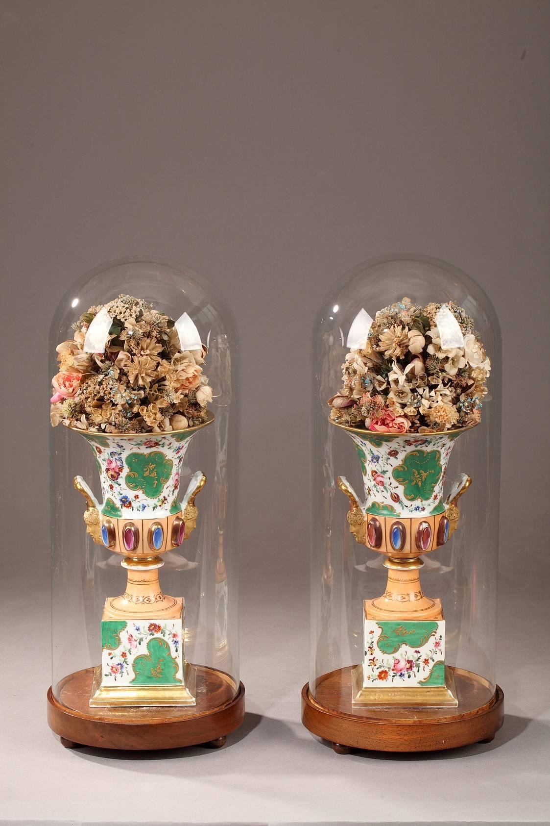 Pair of porcelain Medici vases set on high, square bases. All sides of the vases are decorated with bouquets of multicolored flowers on white background with accents of gold foliage painted on green background. The lower part of the body is
