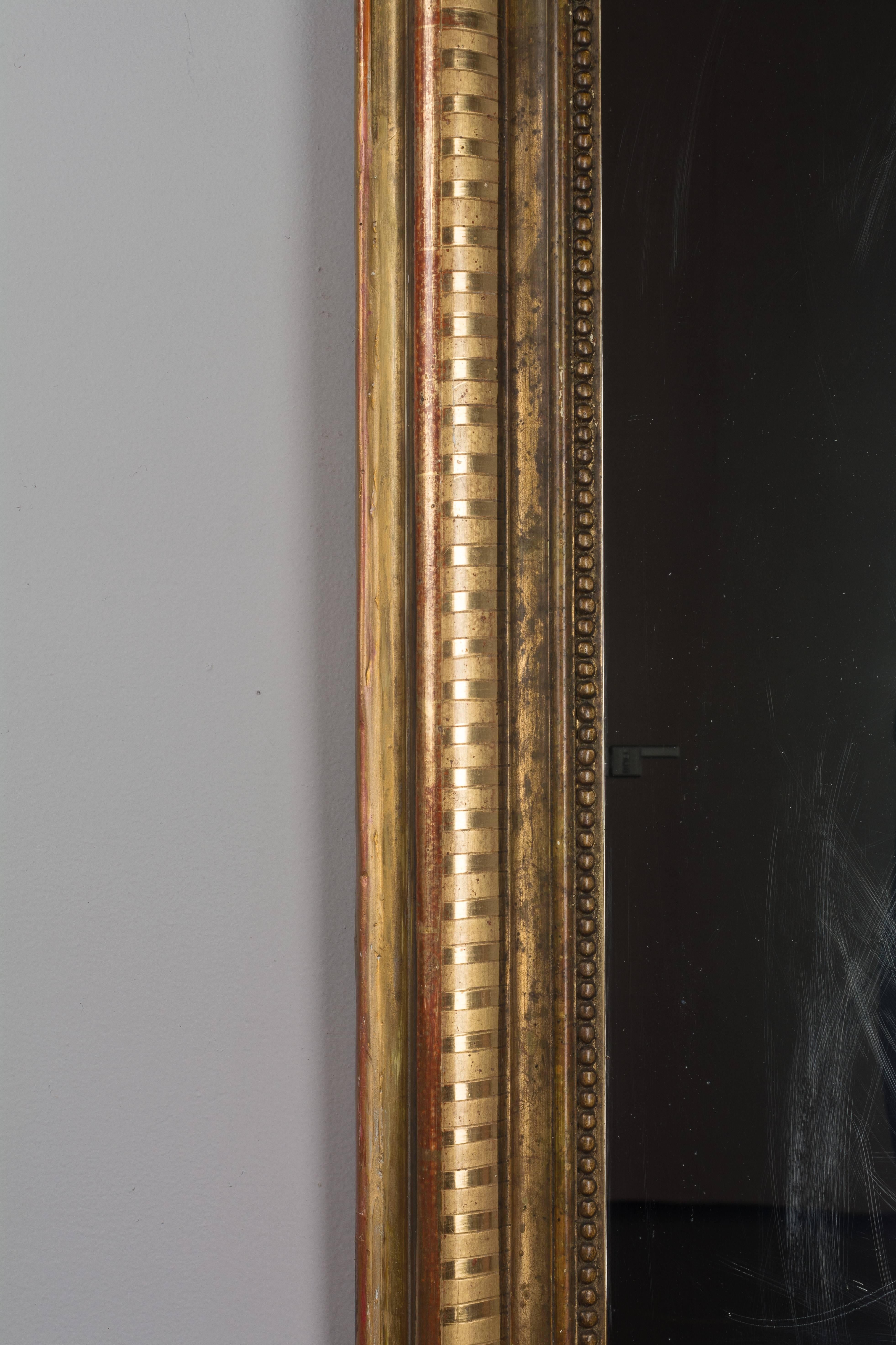 A Louis Philippe giltwood mirror with curved top corners. Warm gilt with ribbed detail. Original mirror with old silvering. Minor loss to gilt and small restorations on edge. Mirror is scratched. Please refer to photos for more details. We have a