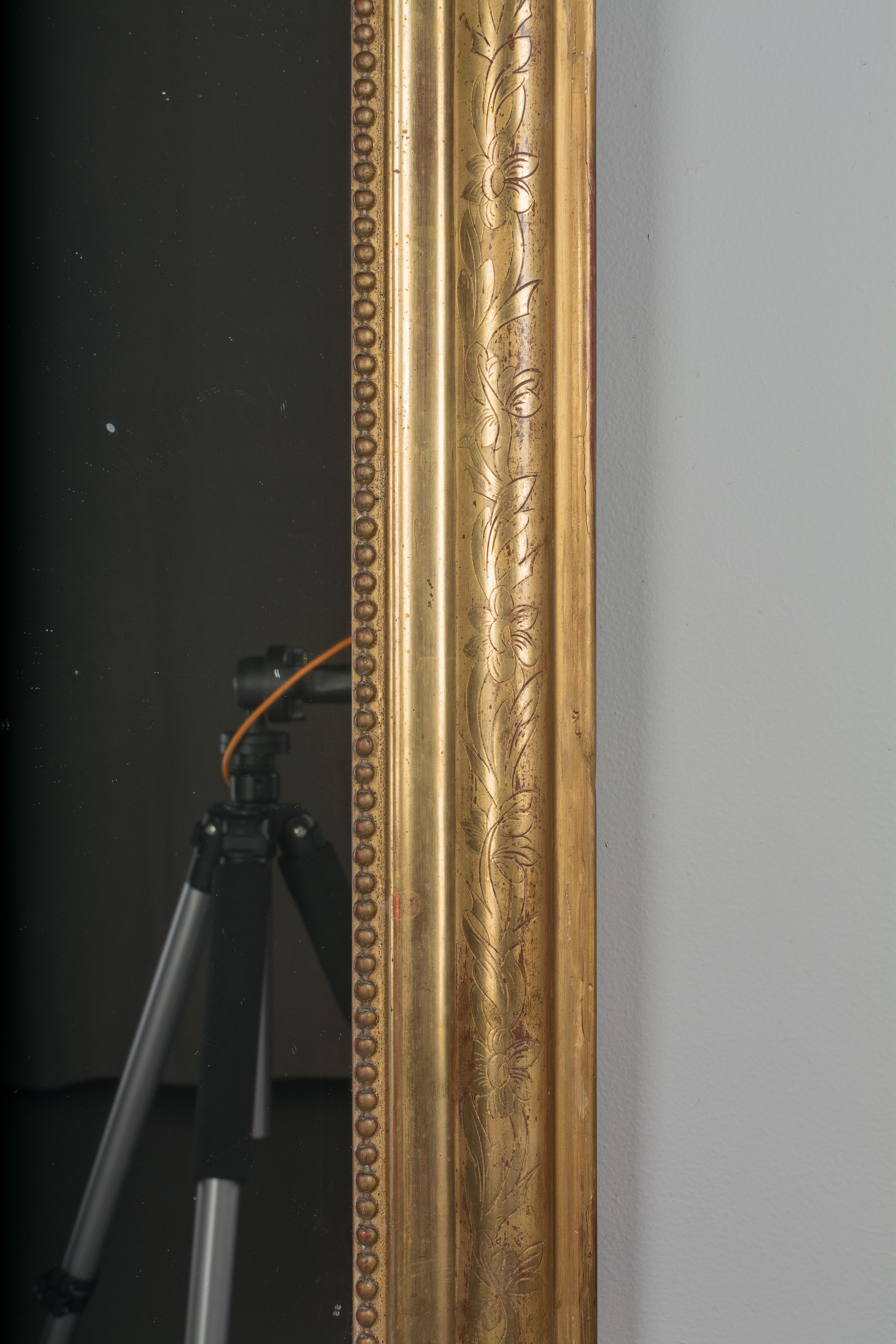 A Louis Philippe style gilded mirror with curved top corners, incised decoration and inner bead border. Warm gilt finish. Original mirror with old silvering. Frame has been restored on the bottom edge.