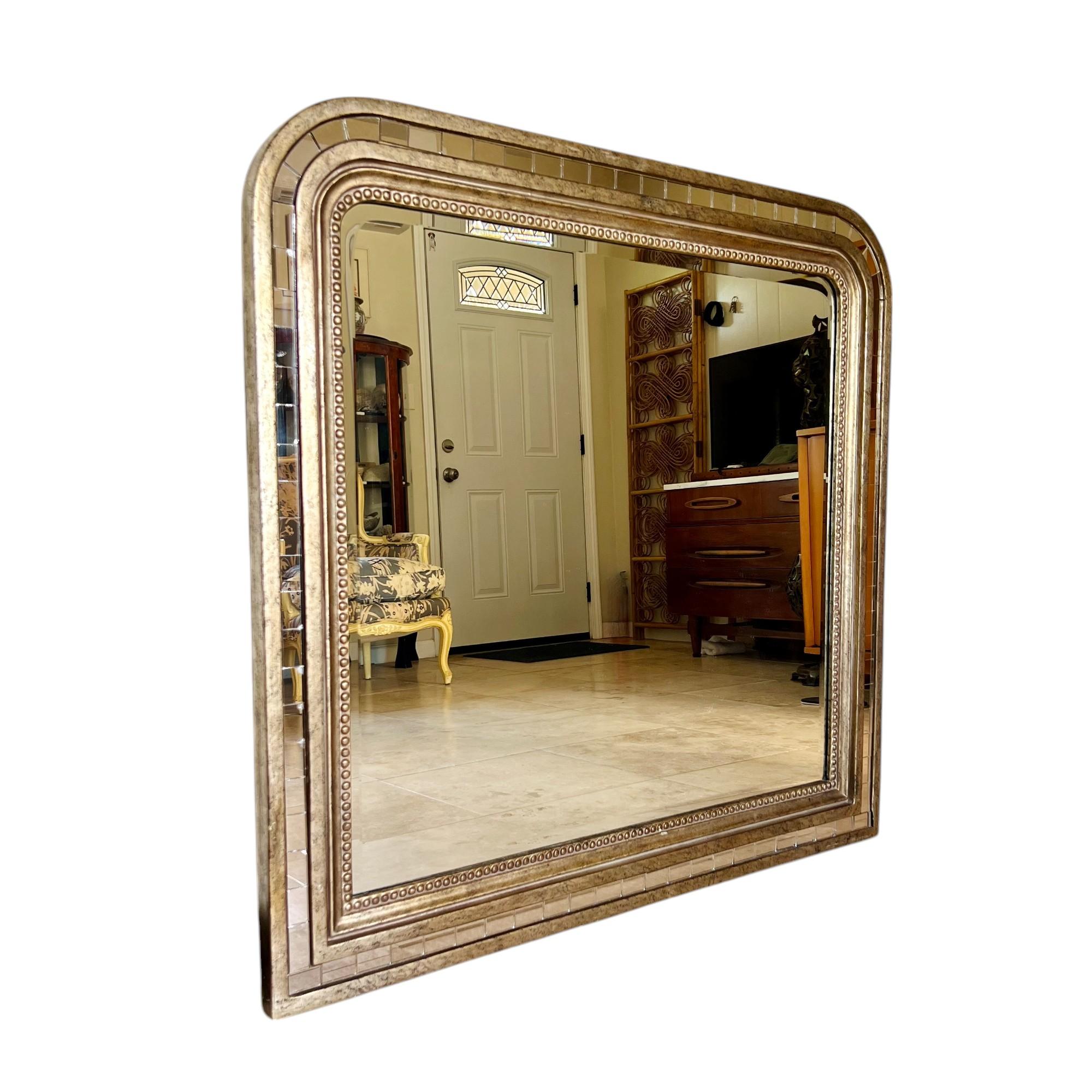 A 21st century Louis Philippe Hollywood regency style overmantel or wall mirror by Raschella Collection circa 2000. This unique piece features curved top corners, a beaded inner border, mirror tile outer border and has an antique light gold finish.