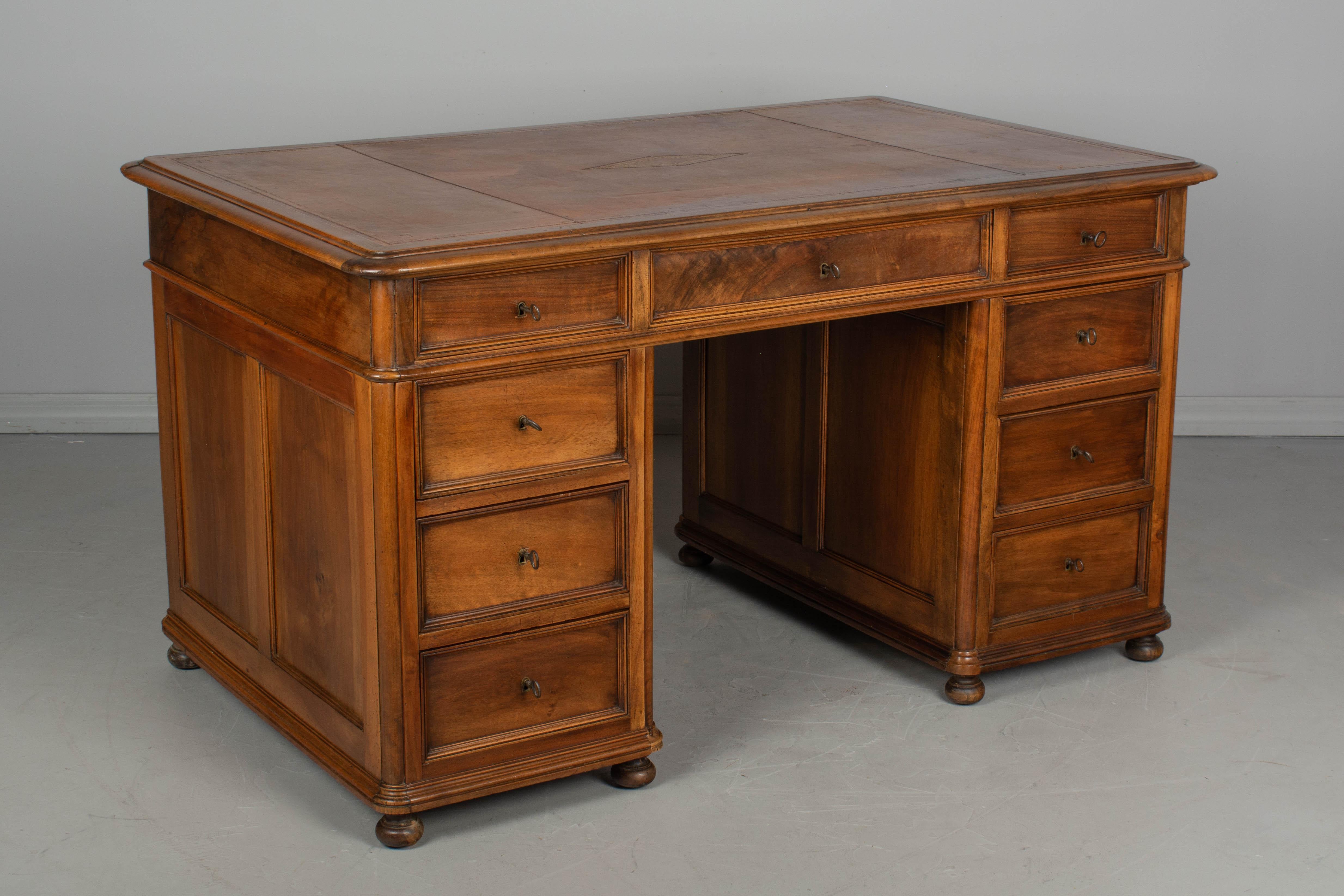 A French Louis-Philippe style partners desk and office chair. This large desk is made of solid walnut and retains the original leather writing surface. Comprised of three parts, the tabletop, with three shallow drawers, rests on top of a pair of