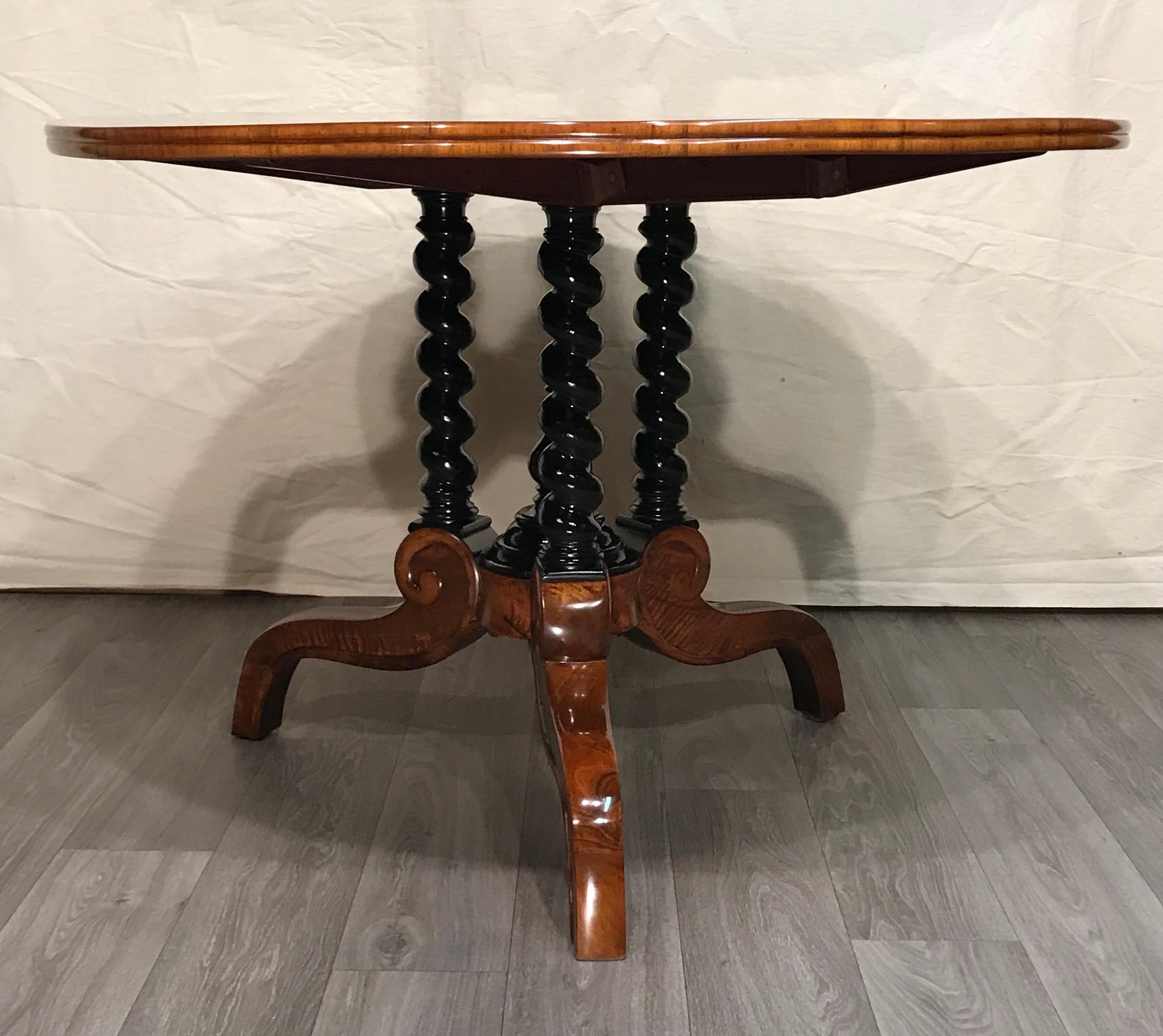 This gorgeous Louis Philippe table dates back to around 1840-50. It stands out for its beautiful walnut root veneer on the top. The base consists of three twisted ebonized columns which stand on a tripod base. The legs of the tripod base are