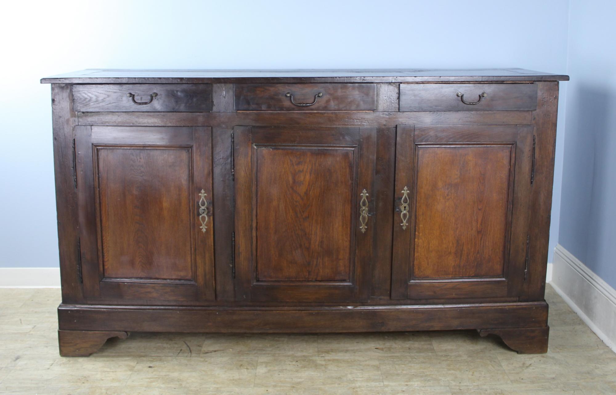 Very good, dark chestnut three-door enfilade with beautiful dark grain highlighted by well colored inset panels on the doors. Glorious glow and patina. Nice stylized feet. The brass hardware is antique, but not original. Excellent storage.