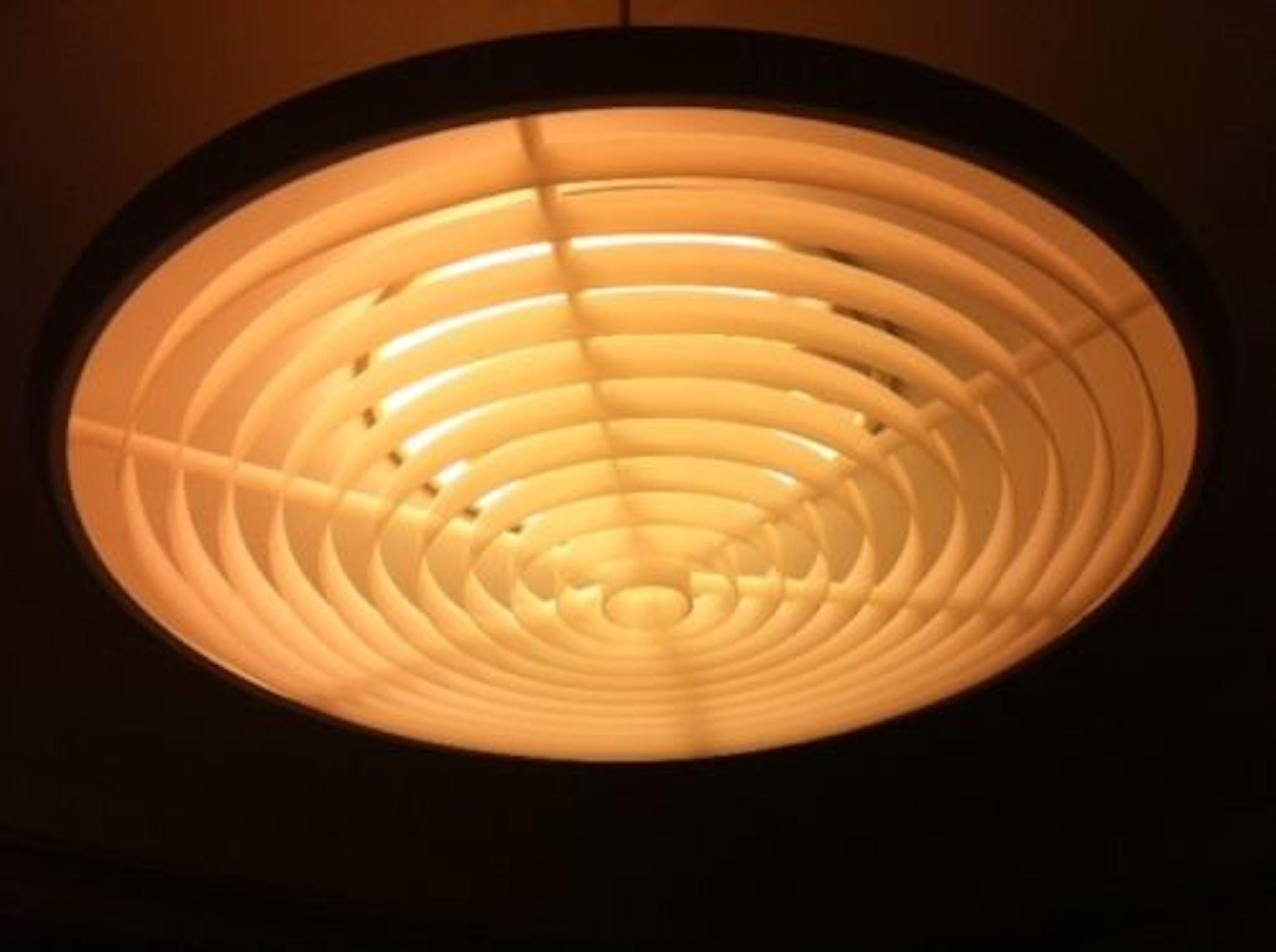 Progettato da Louis Poulsen in Danimarca nel 1967. Si chiama Class Room Pendant Light (Da: Klassependel) ed è composta da un paralume principale in alluminio laccato grigio con un diffusore/distributore di luce in acrilico nella parte inferiore e