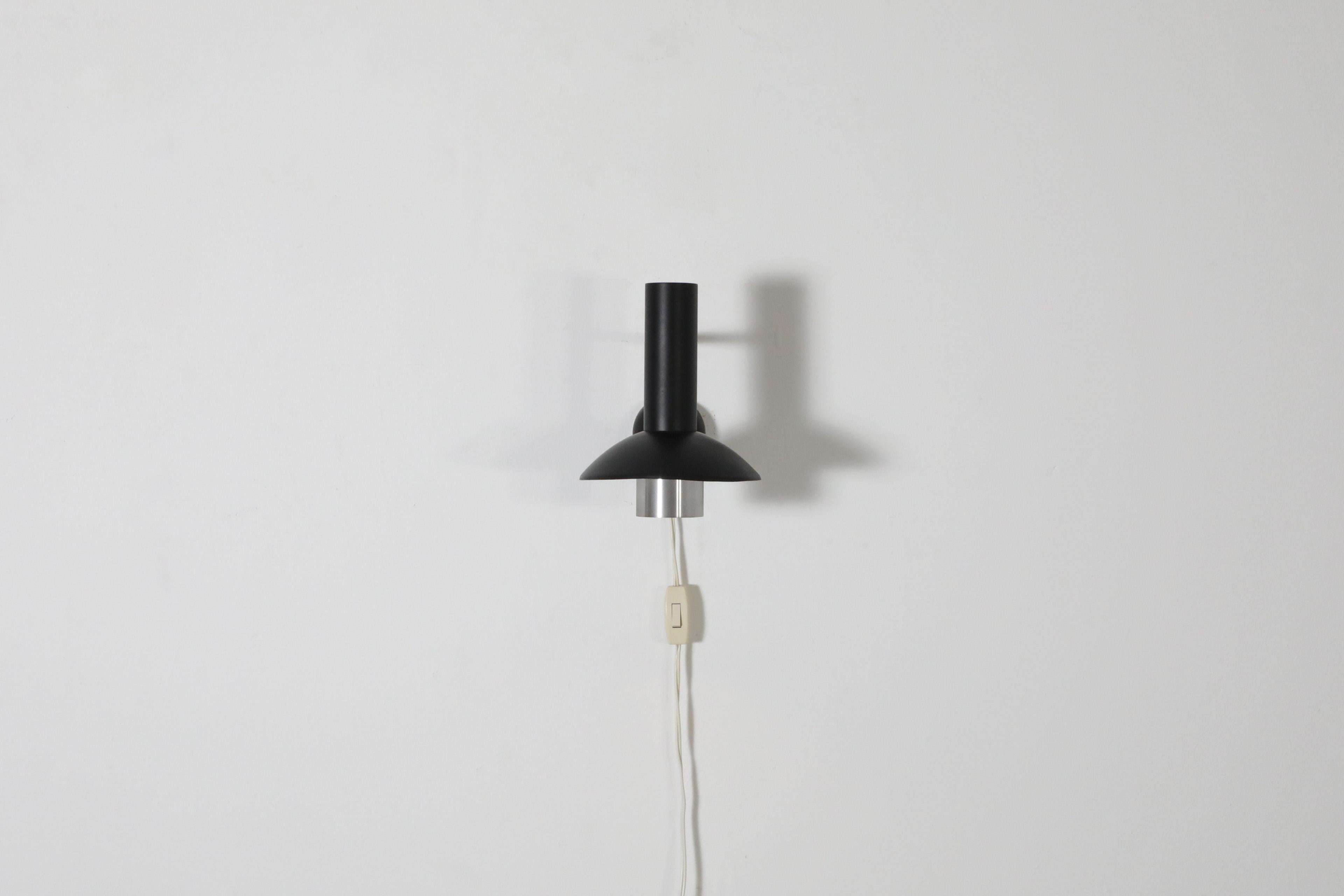 Mid-Century, 1970's, Louis Poulsen designed, 'Louise' wall sconce. Also known as model. 132051. Features a black enameled metal frame with brushed aluminum shade on an adjustable stem. This sleek wall mounted lamp is suitable as a bedside light or