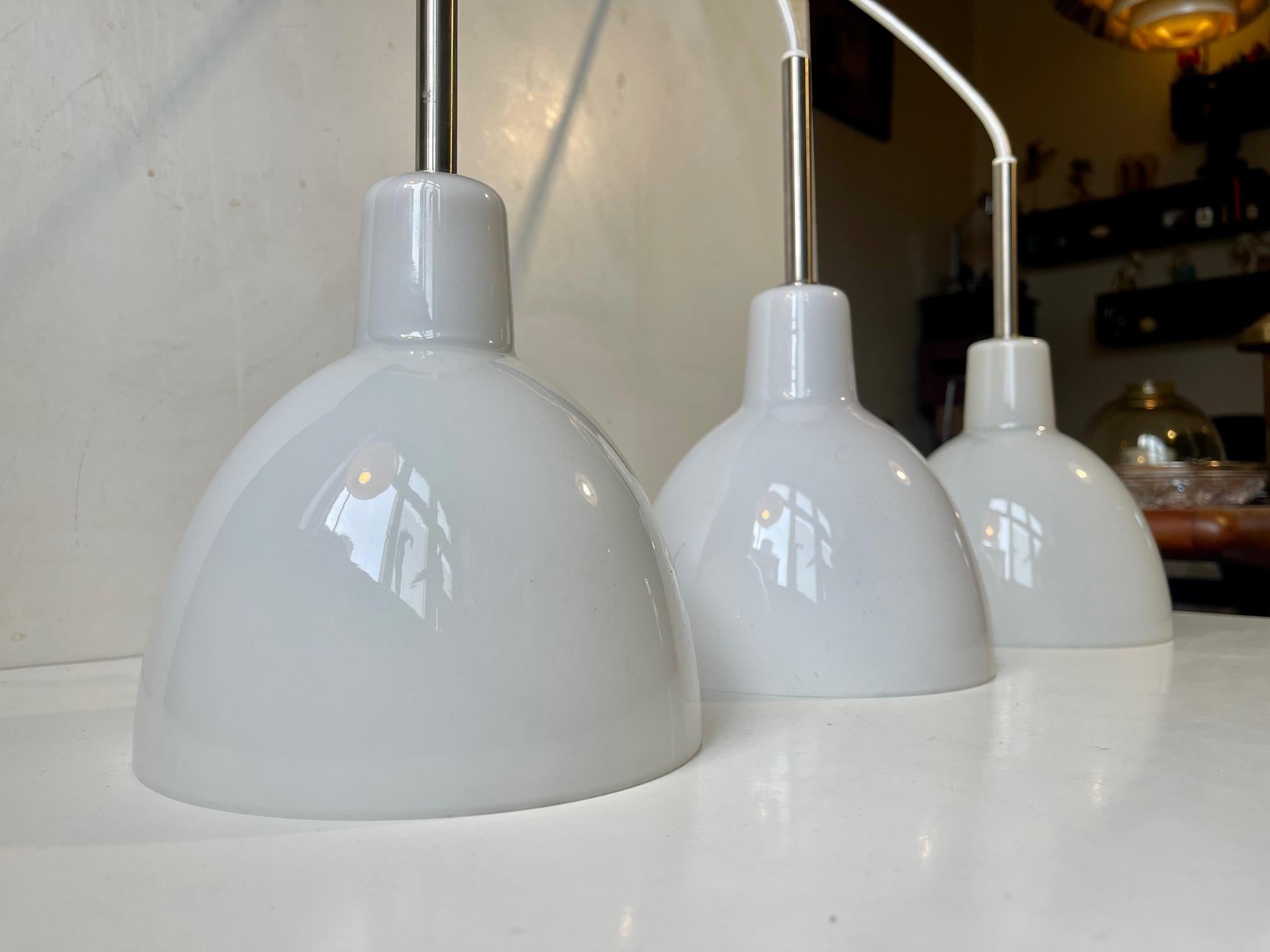 A trio of model 155 Toldbod pendant lamps developed by the design team at Louis Poulsen in 1982. This design is based upon the elliptical reflector of PH - Poul Henningsen. This type of reflector secures a glare-free, uniform and round-symmetrical