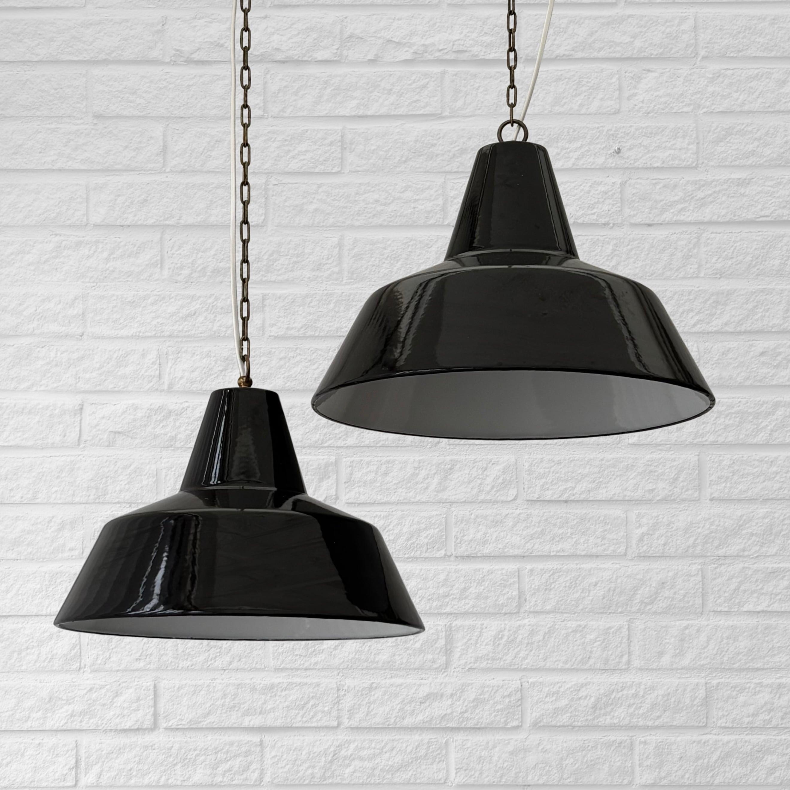 Two early industrial pendant lamps, designed in the 1950s by Axel Wedel Madsen for renowned Danish lighting manufacturer Louis Poulsen. Crafted from enameled steel, they feature a black exterior and a white interior. The lamps come in two different