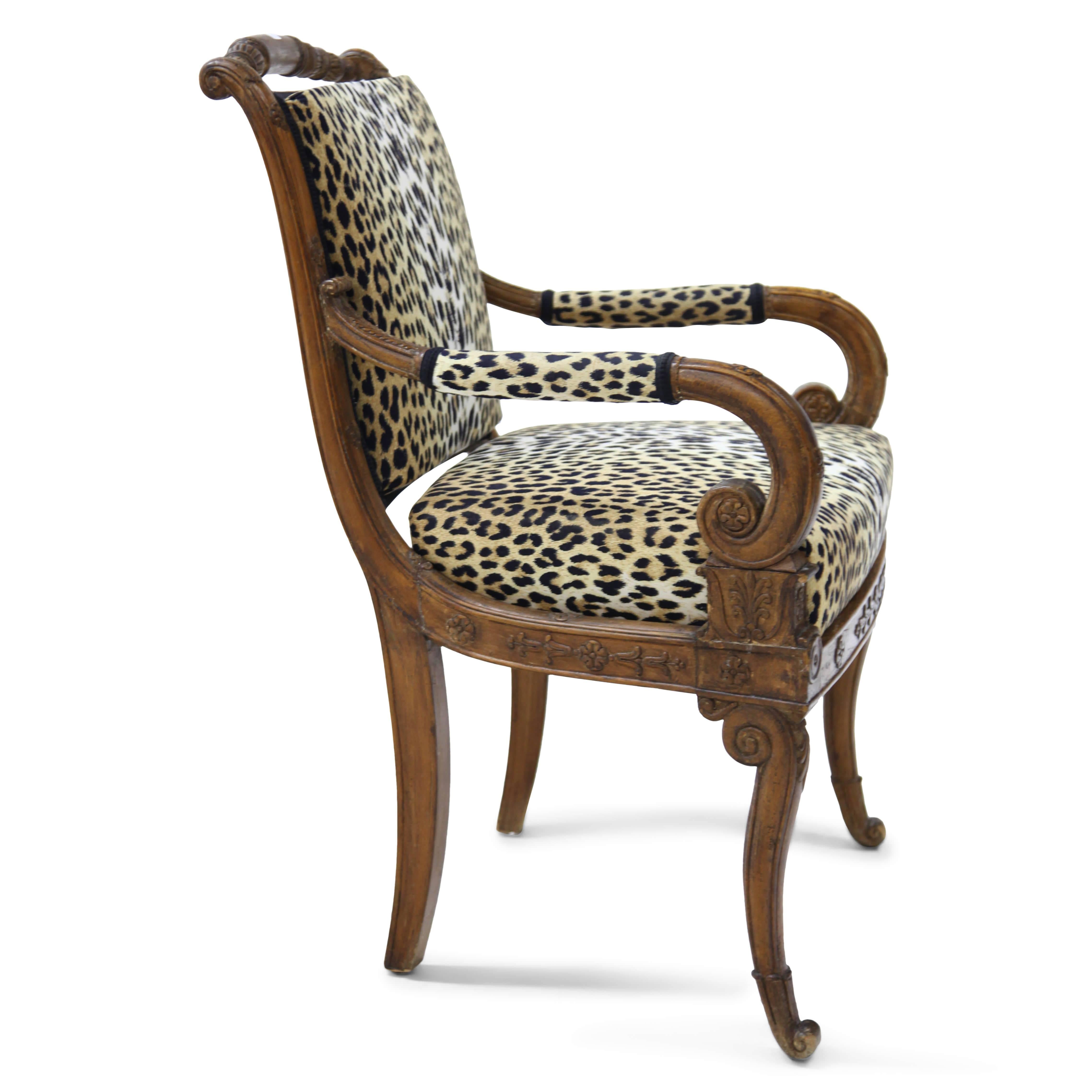Armchair with neoclassical carvings on the railing, the armrests and backrest. The chair stands on volute-shaped feet in the front and slightly curved legs in the back. The armrests end in volutes. Seat and backrest are upholstered with a leopard