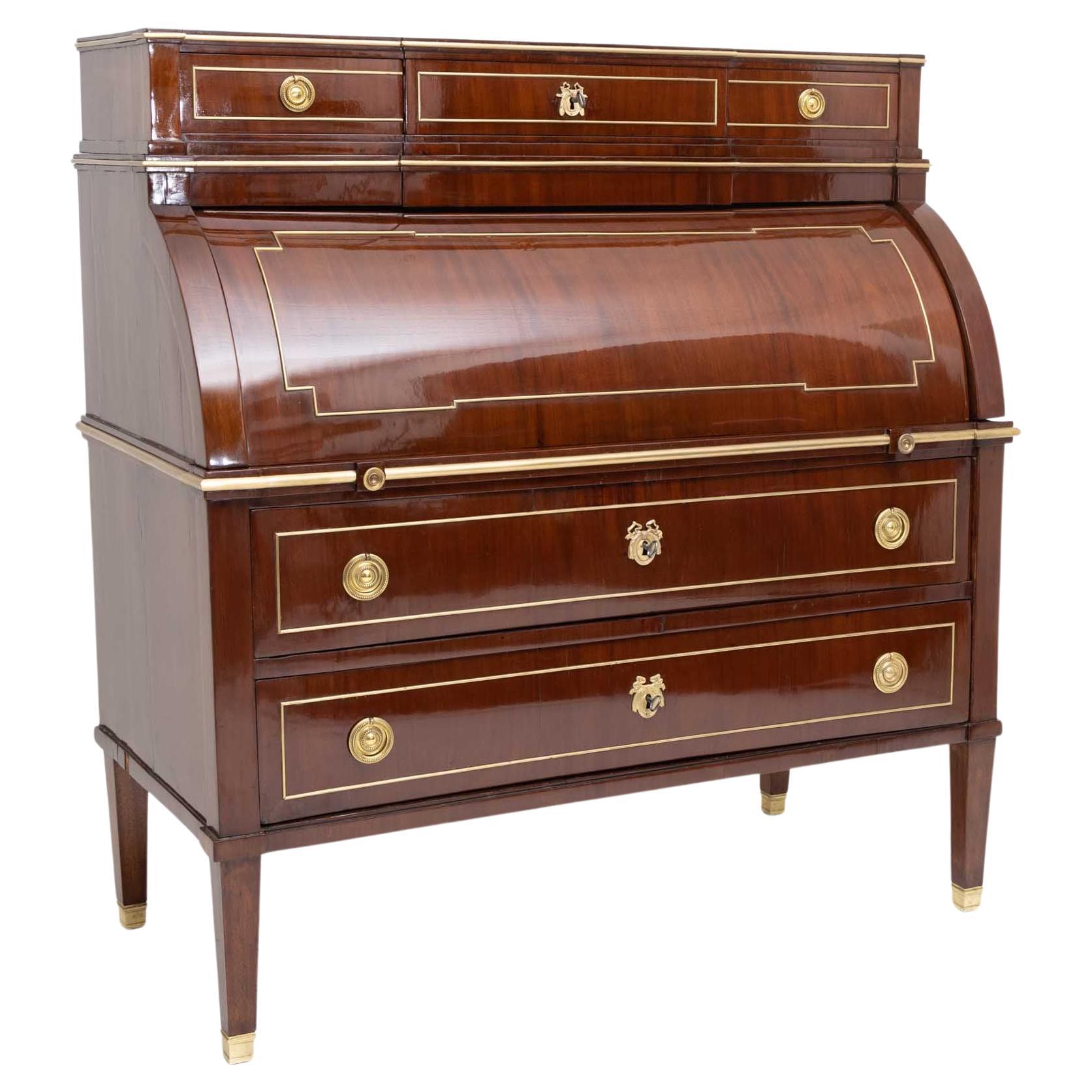 Louis Seize secretaire with mahogany veneer and brass moldings and fittings. The secretaire stands on square tapered legs with brass sabots and has three wide drawers, the top one protruding risalite-like in the center. The interior layout consists