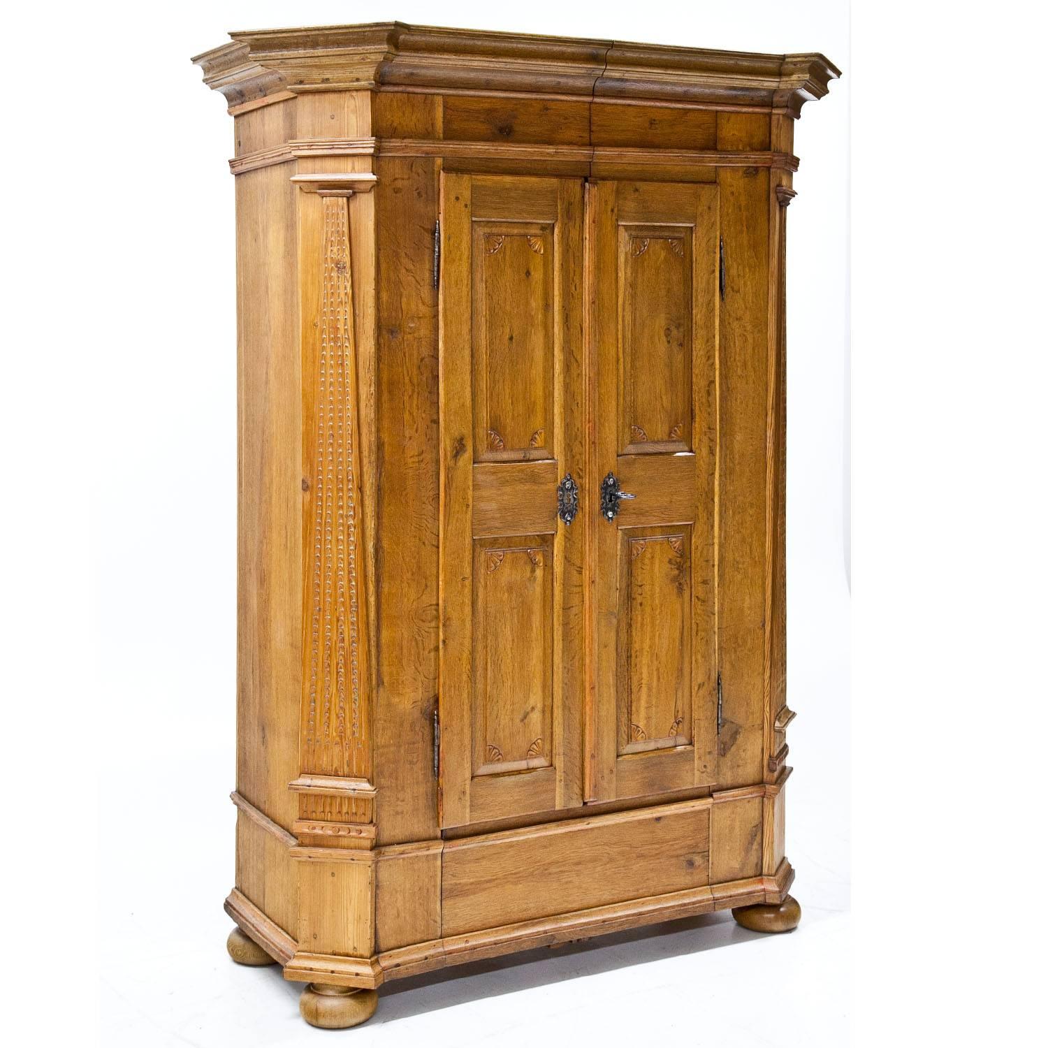 Two-doored cabinet standing on bun feet with slanted corners a profiled cornice and pyramidal pilasters. The doors with fillings and carved shell ornaments in each corner.