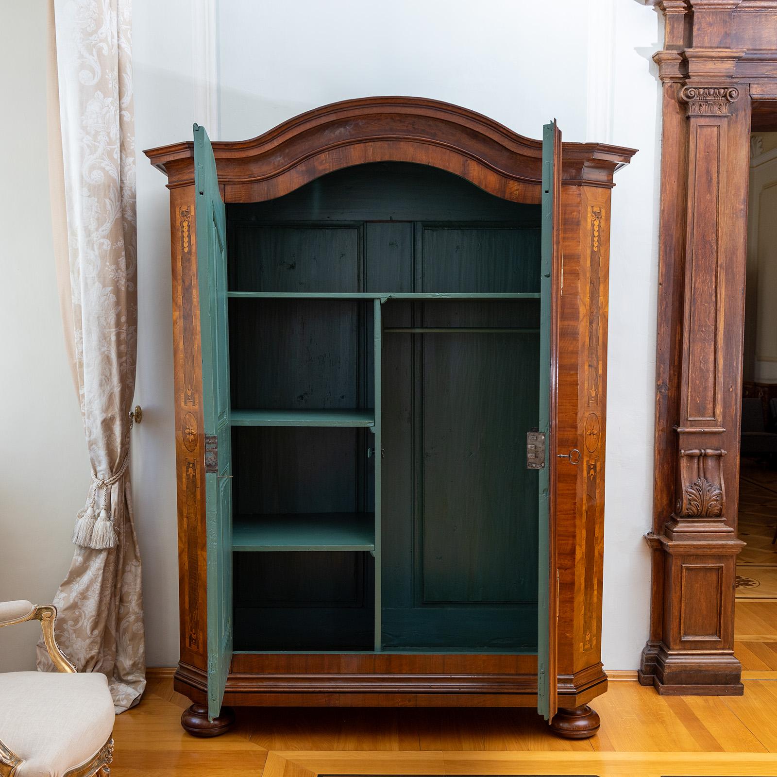Gran armario Louis Seize de dos puertas con esquinas biseladas y cornisa perfilada y curvada. El mueble se apoya en pies de bola moldeados y está chapado en nogal. Grandes medallones de bronce dorado adornan las bocallaves. El interior, pintado de