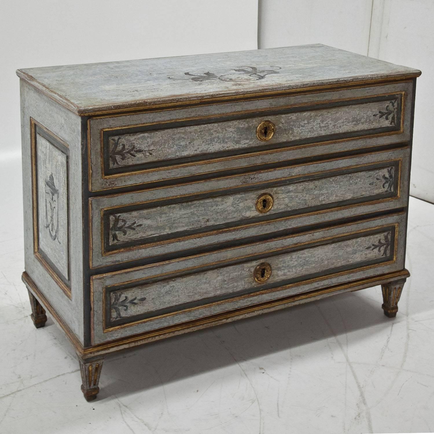 Three-drawered, blue Louis Seize chest of drawers on short fluted feet. The fillings on the front and on the sides show some historical designs and are partly gilt. The chest was repainted and has an aged finish.