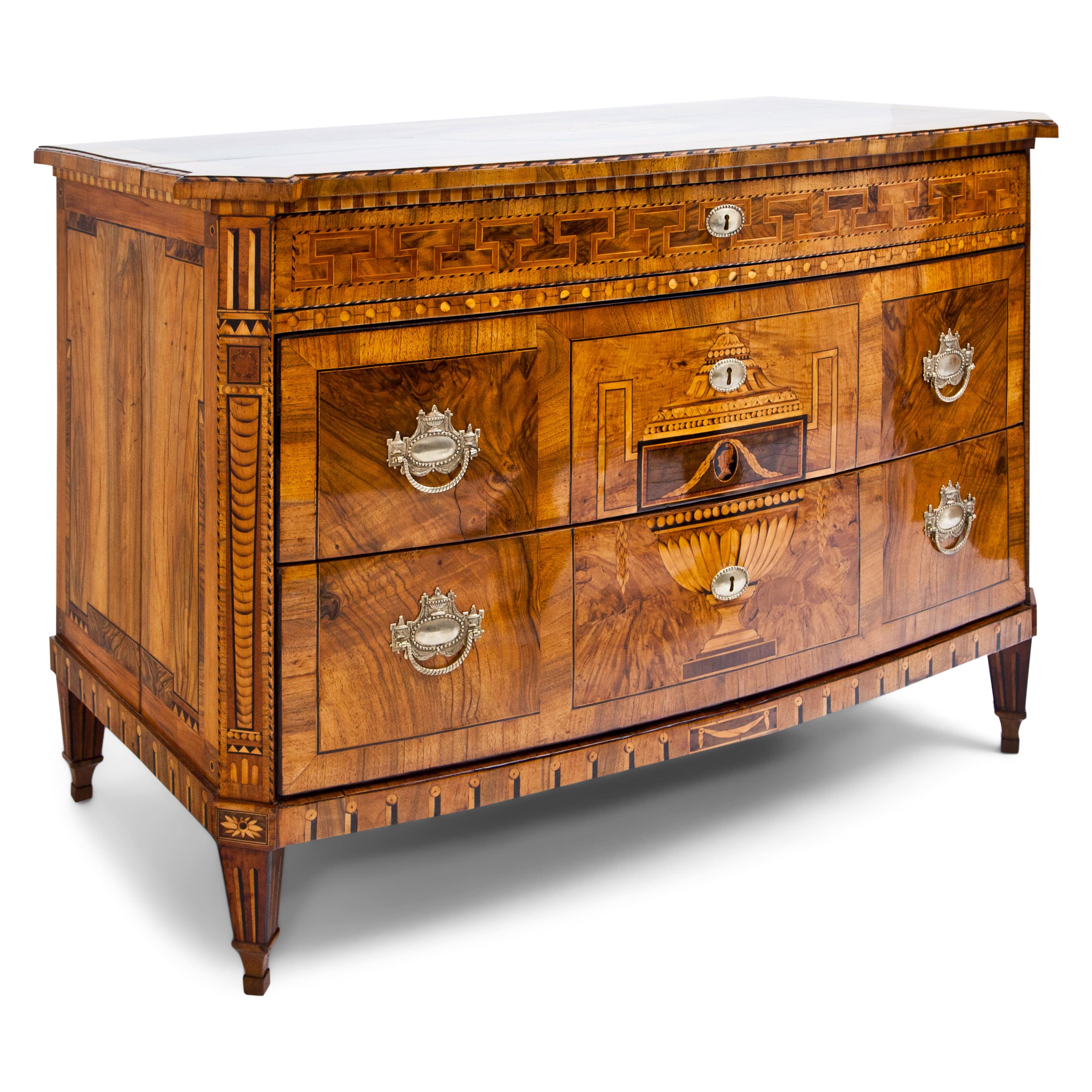 Three-drawered Dresden chest of drawers on square pointed feet with a bow front and bevelled corners. The two lower drawers are constructed without a traverse and are visually divided into three sections. The large-format representation of an