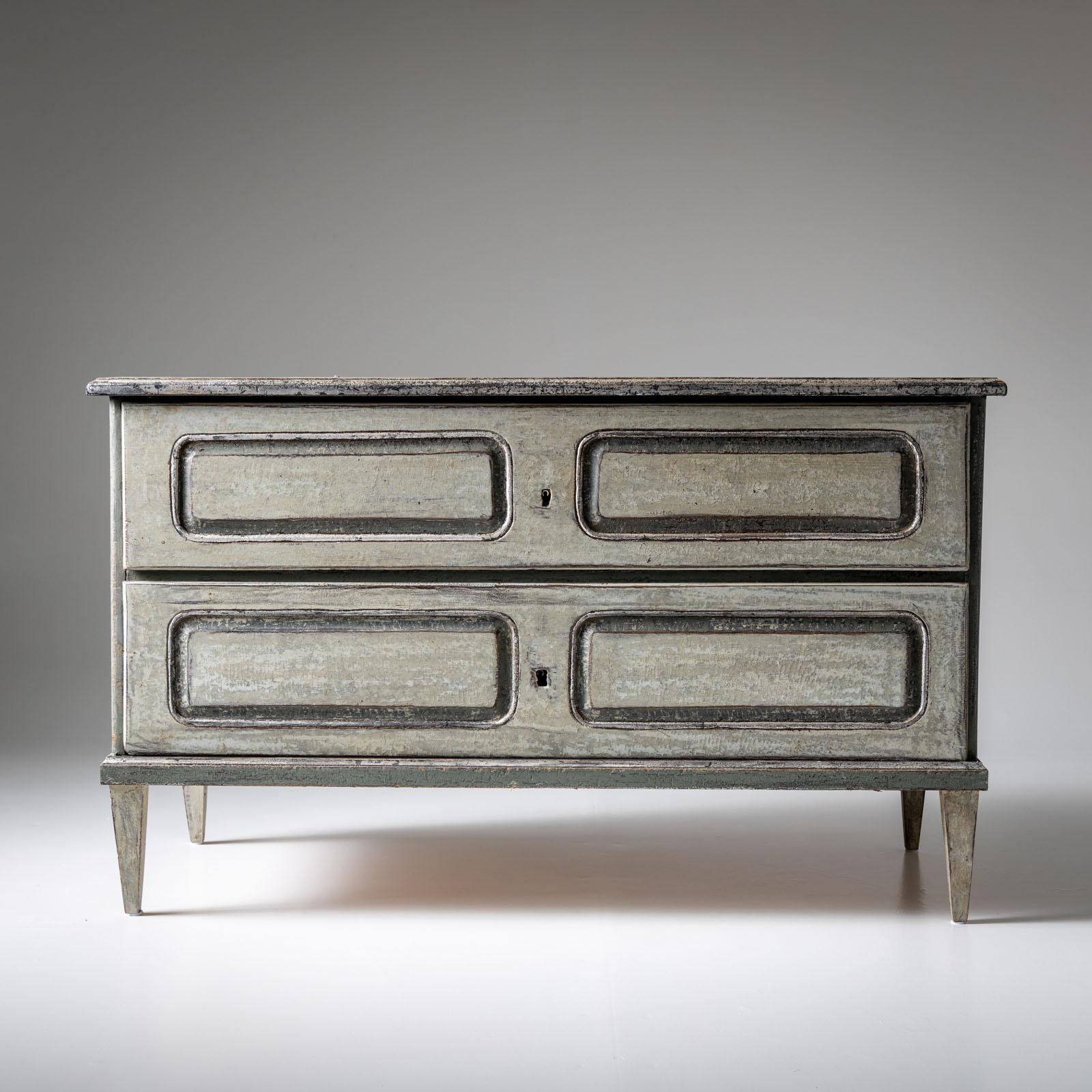 Large two-drawer chest of drawers with square tapered legs and panels featuring rounded corners. Recently painted in a light green hue with a hint of silver patina in select areas, it exudes a subtle vintage charm. The antique finish applied to the