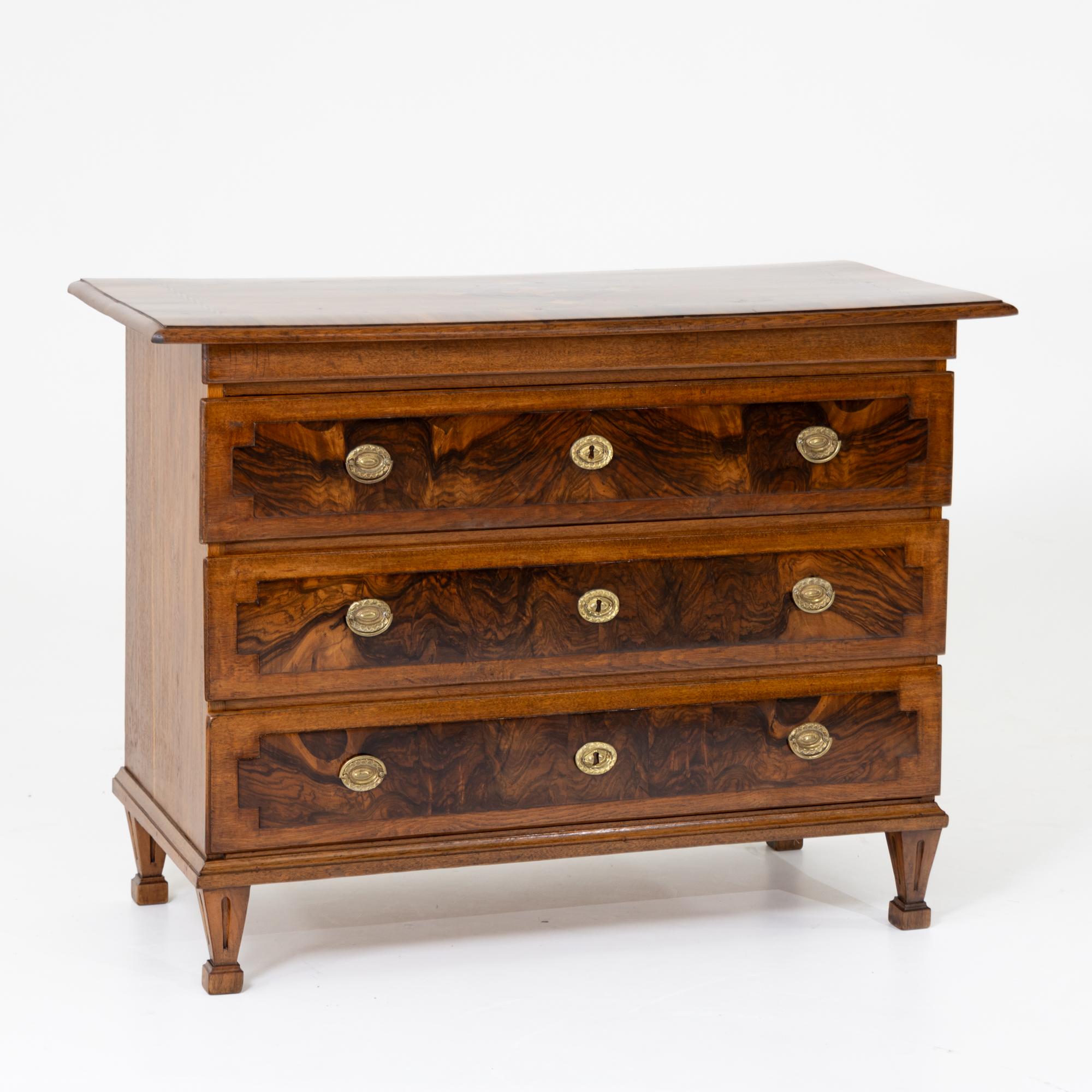 Cassettiera Louis Seize in Oak con tre cassetti e piedi quadrati a punta. La cassettiera è incastonata in radica sul davanti e il piano presenta intarsi a forma di fasce e un motivo centrale a diamante realizzato con legni diversi, in parte