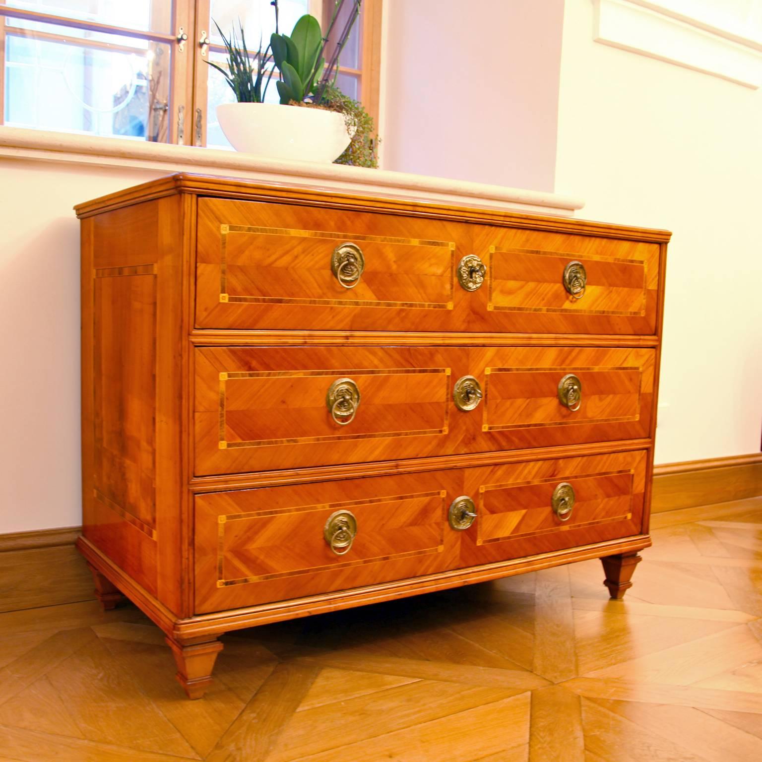 Three-drawered Louis Seize chest of drawers on profiled tapered feet. The chest shows a very beautiful cheerywood veneer pattern with framing inlays on the top, sides and on the front.