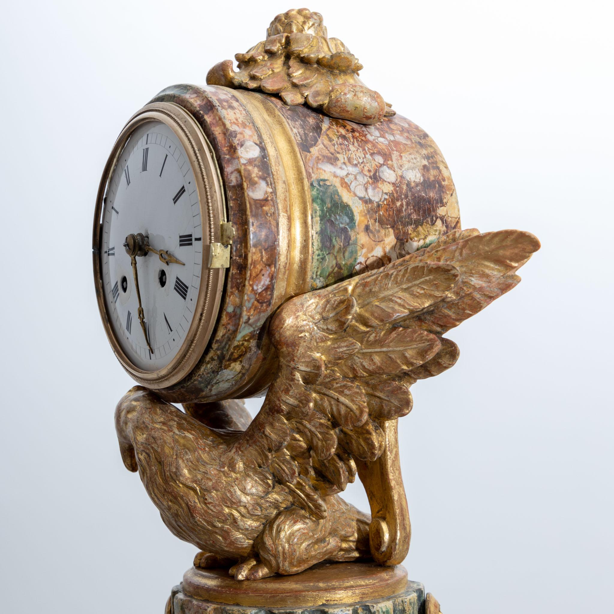 A patinated wooden pendulum on a fluted column stump with festoons and carved eagle decoration, which supports the cylindrical clock case with enamel dial between its stretched wings.