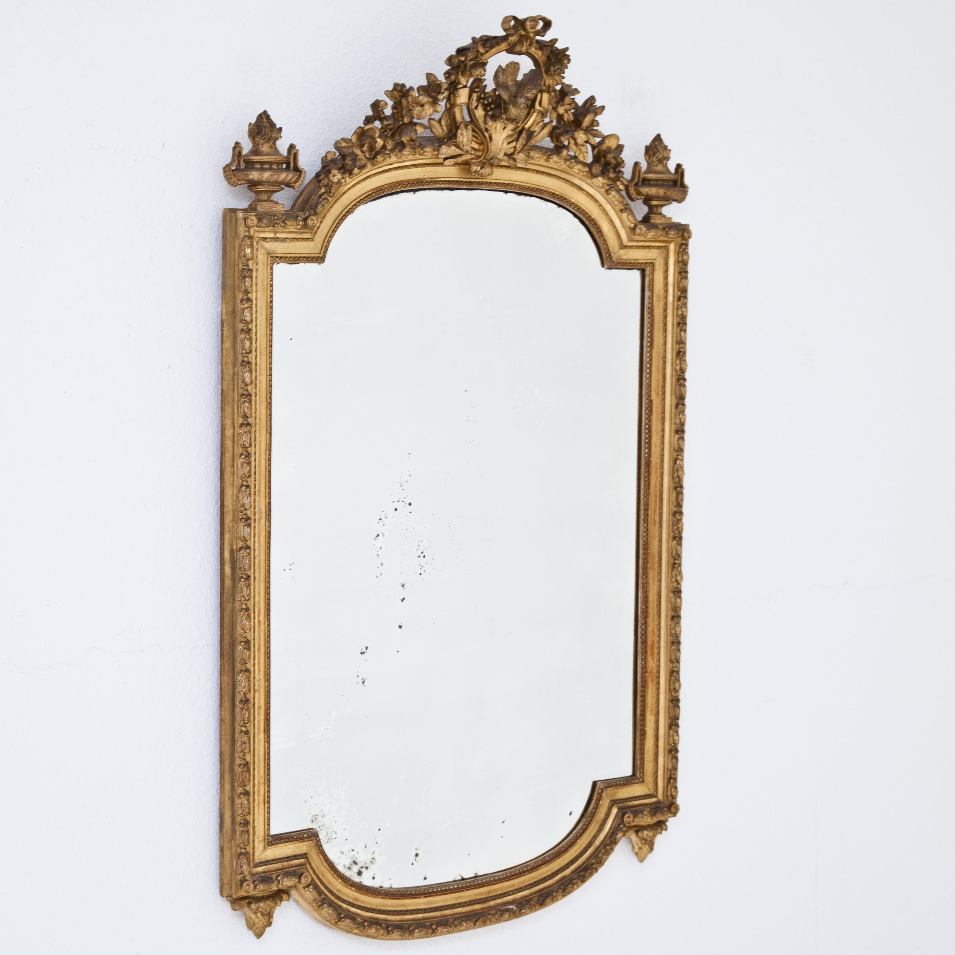 Wall mirror with gilded, carved frame and top with dovetail decoration, festoons and urns.
  