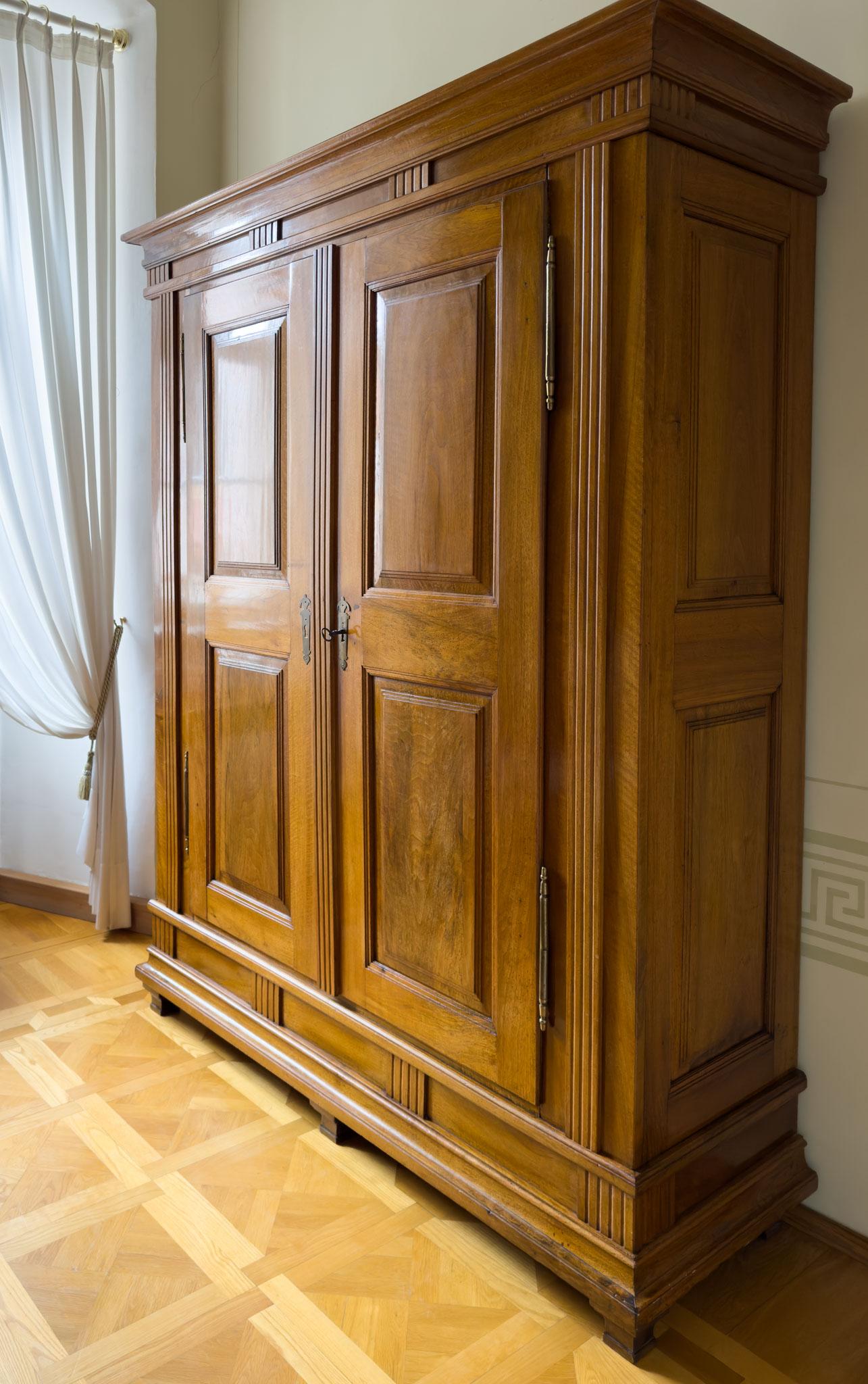 Two-door wardrobe in walnut with coffered doors and sides and fluted pilaster elements as well as a profiled cornice. The wardrobe stands on low socketed pointed feet with a high plinth zone. Iron bar lock with rotating shackle.
