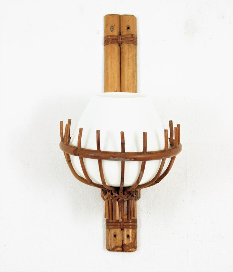 Large rattan and bamboo wall light with milk glass lampshade. Attributed to Louis Sognot. France, 1950s.
This lantern wall light has a clean design. The bamboo bamboo backplate holds a milk glass shade beautifully suspended on a rattan