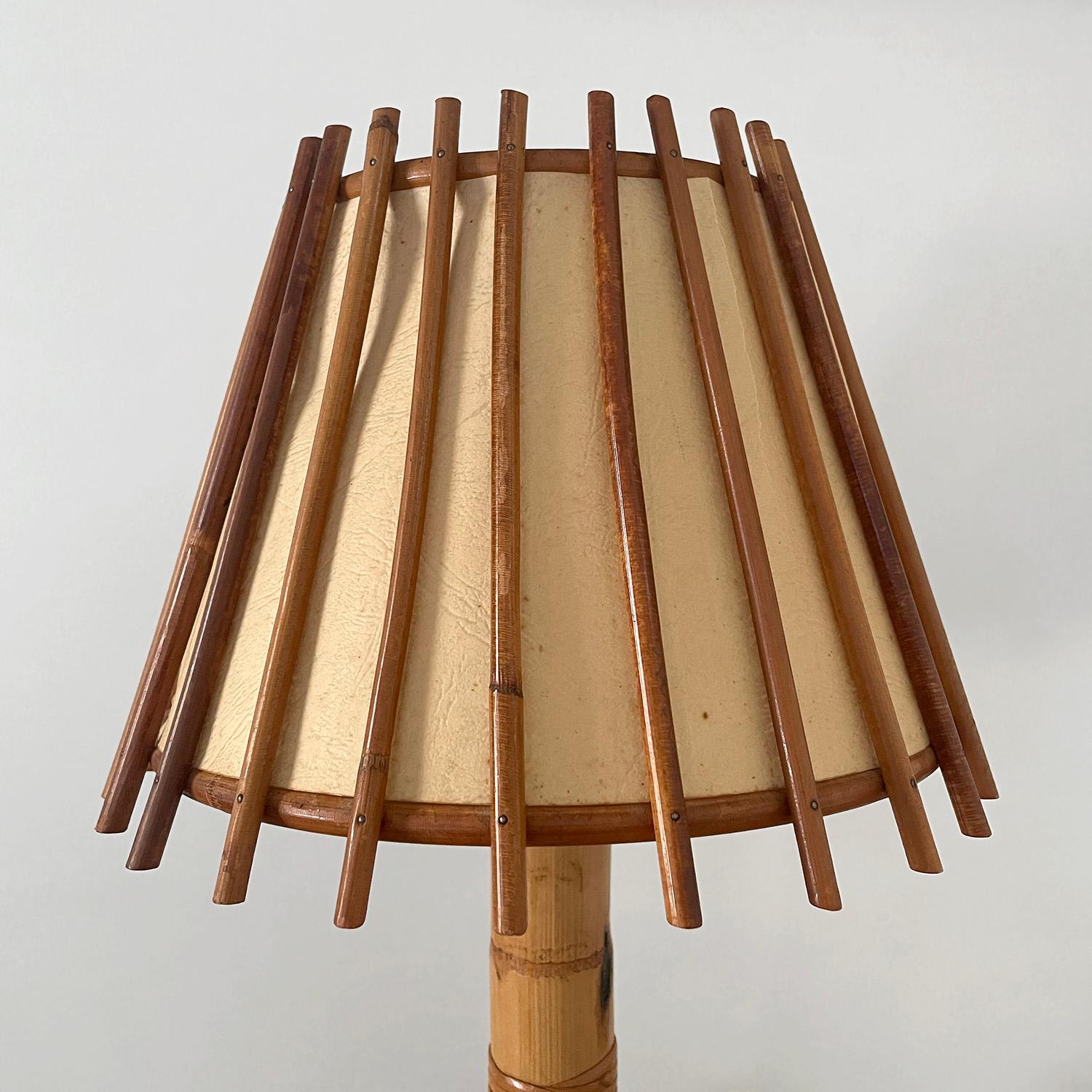 Lampe de table en bambou et rotin Louis Sognot
France, vers 1960
Composition et toucher organiques 
Base en bambou sculpté 
L'abat-jour est constitué de roseaux de rotin verticaux avec des rivets cloutés.
Les cartons d'ombrage d'origine présentent