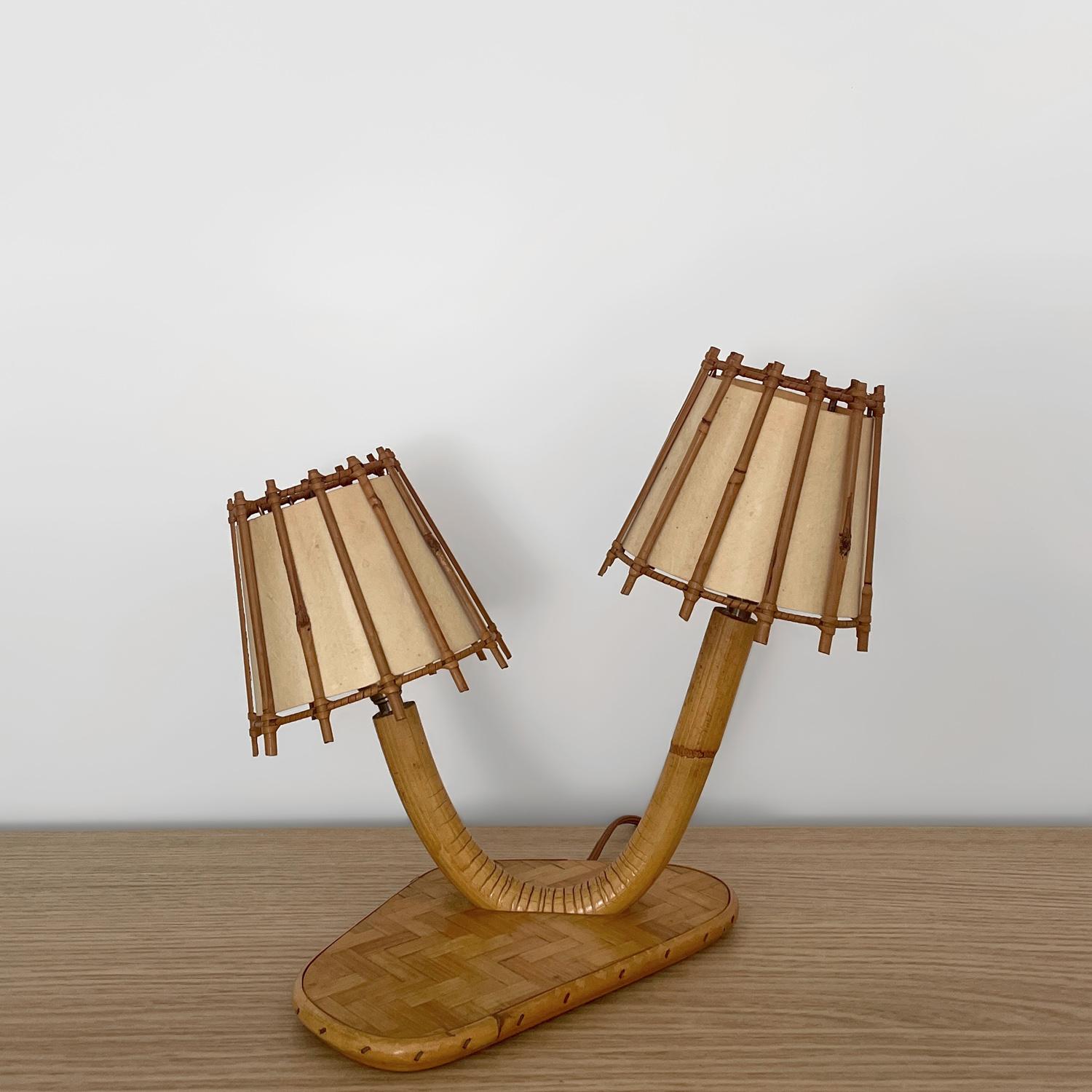 Lámpara de mesa doble Louis Sognot de ratán francés y bambú
Francia, hacia 1960
Pieza artesanal hecha a mano
¡Esta encantadora lámpara nos hace sonreír! 
El bambú bellamente esculpido es la pieza central de esta lámpara doble
Cada pantalla está