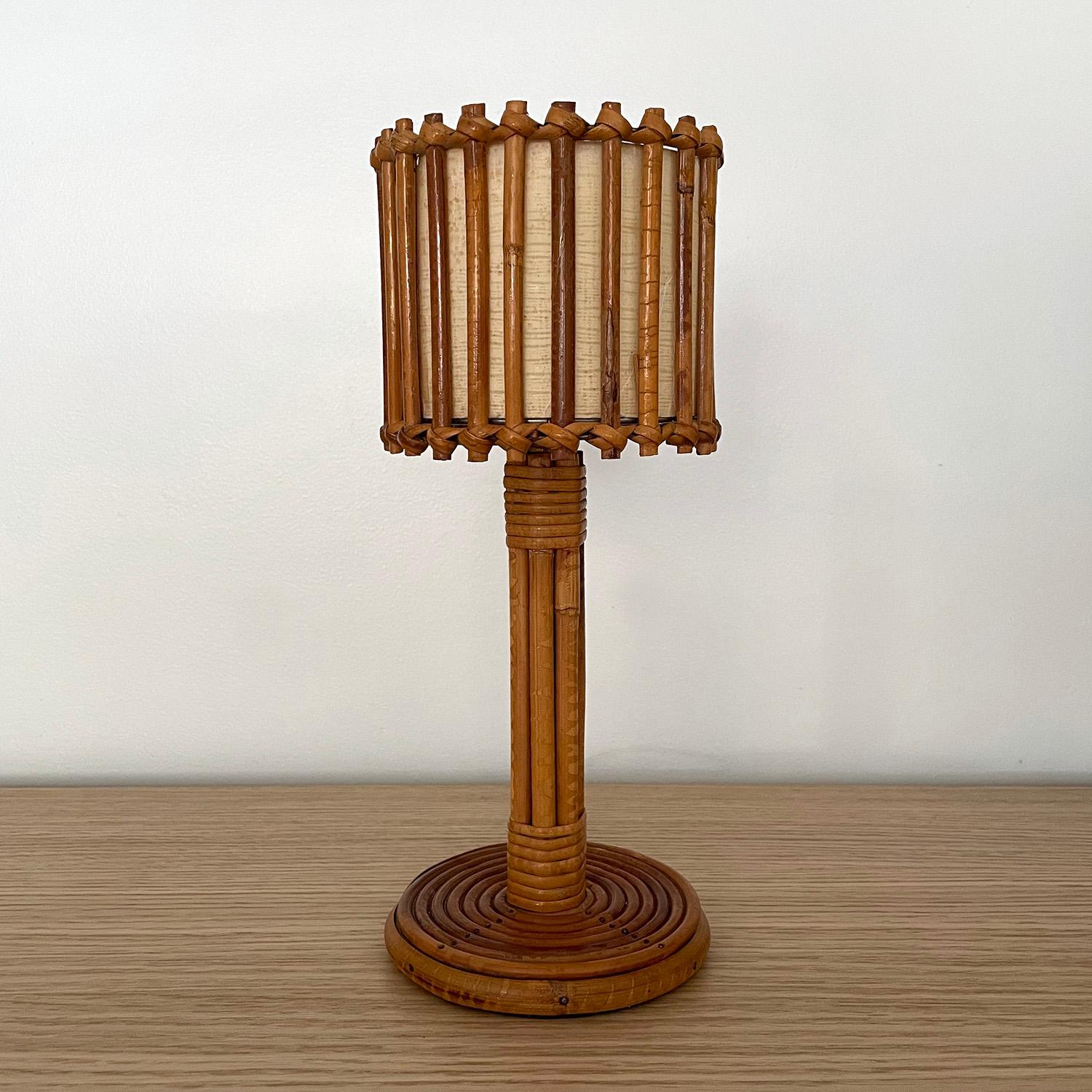 Lampe à poser en rotin Louis Sognot
France, vers les années 1960
Les roseaux de rotin verticaux sont tissés de manière complexe autour de l'abat-jour en forme de tambour.
La doublure intérieure en lin d'origine présente de légères marques de surface