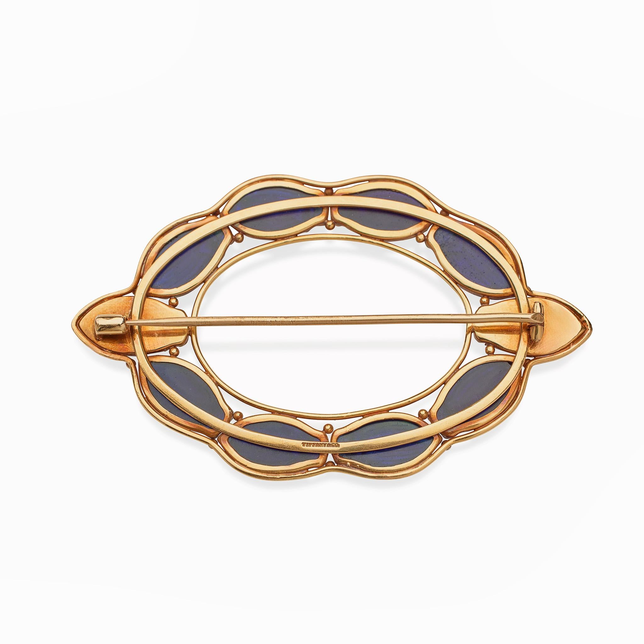 This Louis Tiffany brooch dating from circa 1909 is composed of favrile glass scarabs and gold. The oval form is bezel-set with 10 glass scarabs with iridescent blue, indigo and green tones, within a delicate wire mount highlighted by gold