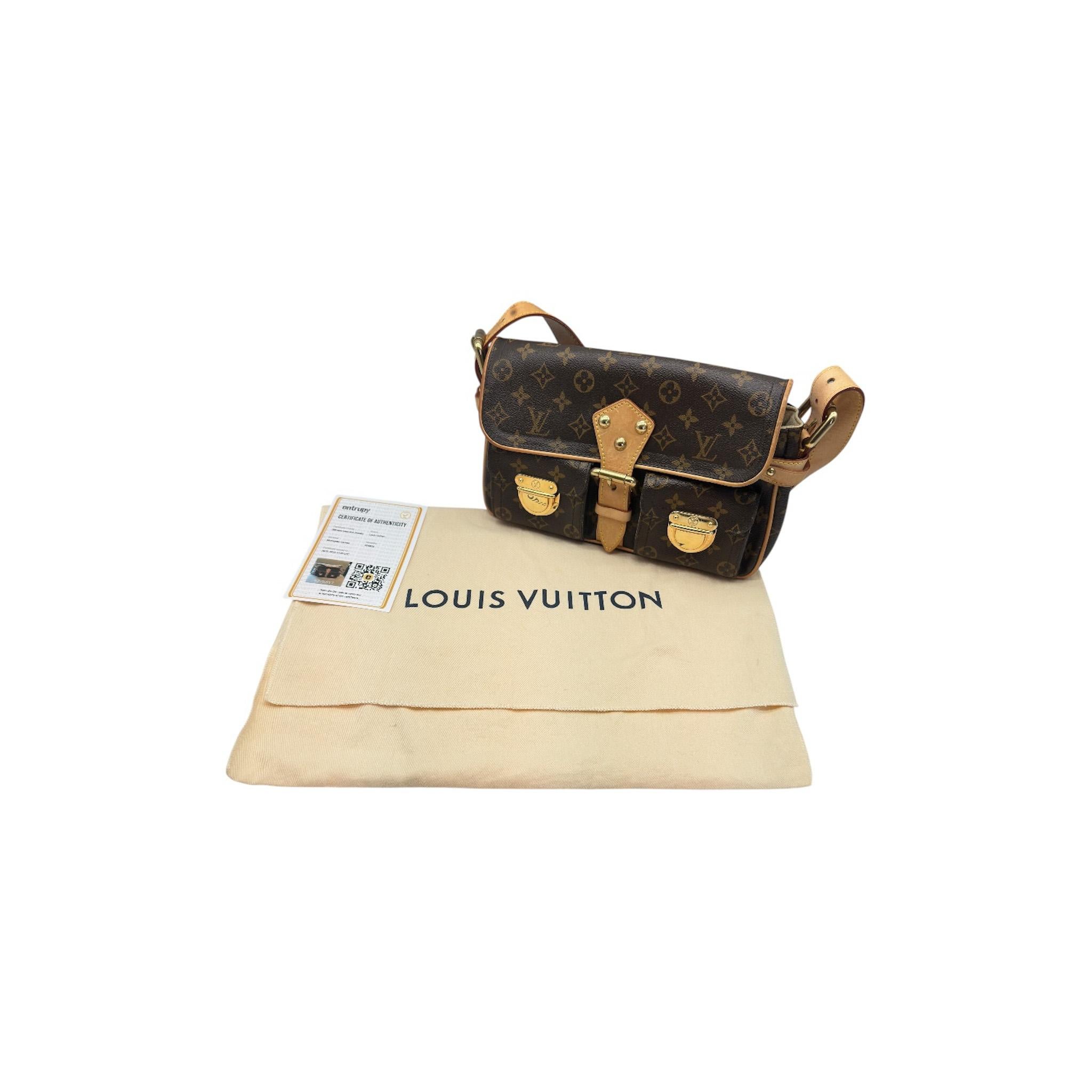 El Bolso de hombro Louis Vuitton Monograma Hudson PM de la colección 2005 de Marc Jacobs presenta la clásica lona Monograma marrón con ribetes de piel vachetta. Tiene una correa de piel ajustable, herrajes de latón pulido, dos bolsillos delanteros y