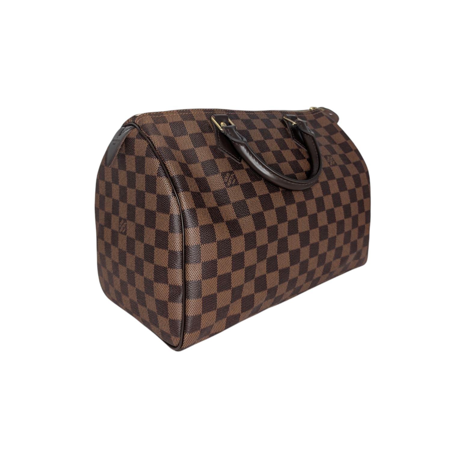 This Louis Vuitton Speedy 30 was made in the USA and it is finely crafted of the classic Louis Vuitton Damier Ebene coated canvas with leather trimming and gold-tone hardware features. It has dual rolled leather top handles and a single zipper