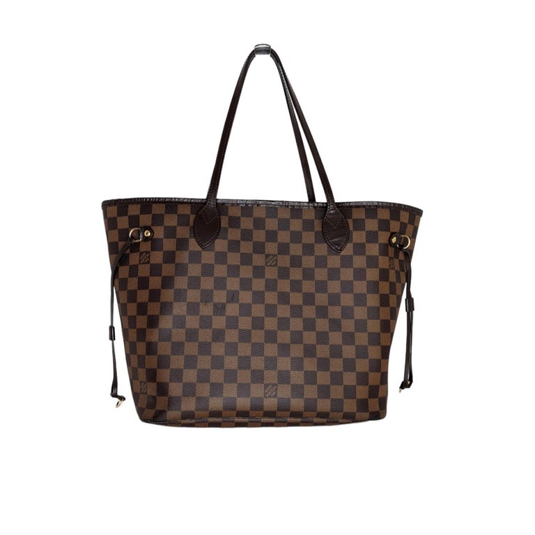 This chic handbag is crafted of classic Louis Vuitton Damier coated canvas in brown. The bag features chocolate brown cowhide leather shoulder straps, side cinch cords, and trim, with polished brass hardware. The top is open to a striped red fabric