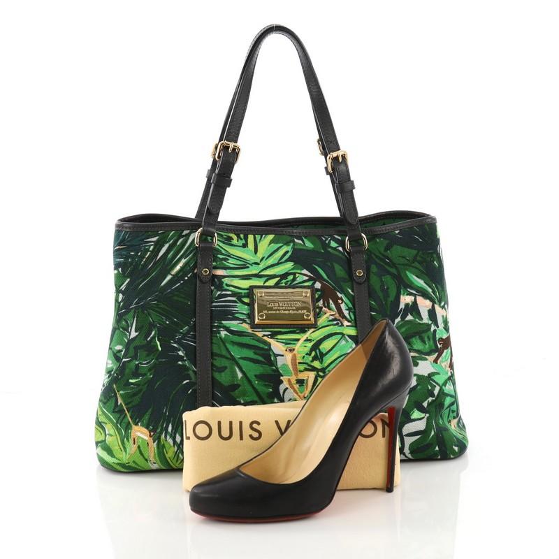 This Louis Vuitton Ailleurs Cabas Limited Edition Printed Canvas PM, crafted from green printed canvas, features a tropical jungle scene print, dual adjustable flat leather handles, protective base studs, and gold-tone hardware. Its hook clasp