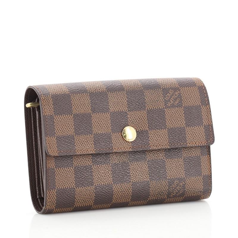 This Louis Vuitton Alexandra Wallet Damier, crafted from damier ebene coated canvas, features leather trim and gold-tone hardware. Its snap button closure opens to a brown leather interior with multiple card slots, zip pocket, and slip pockets.