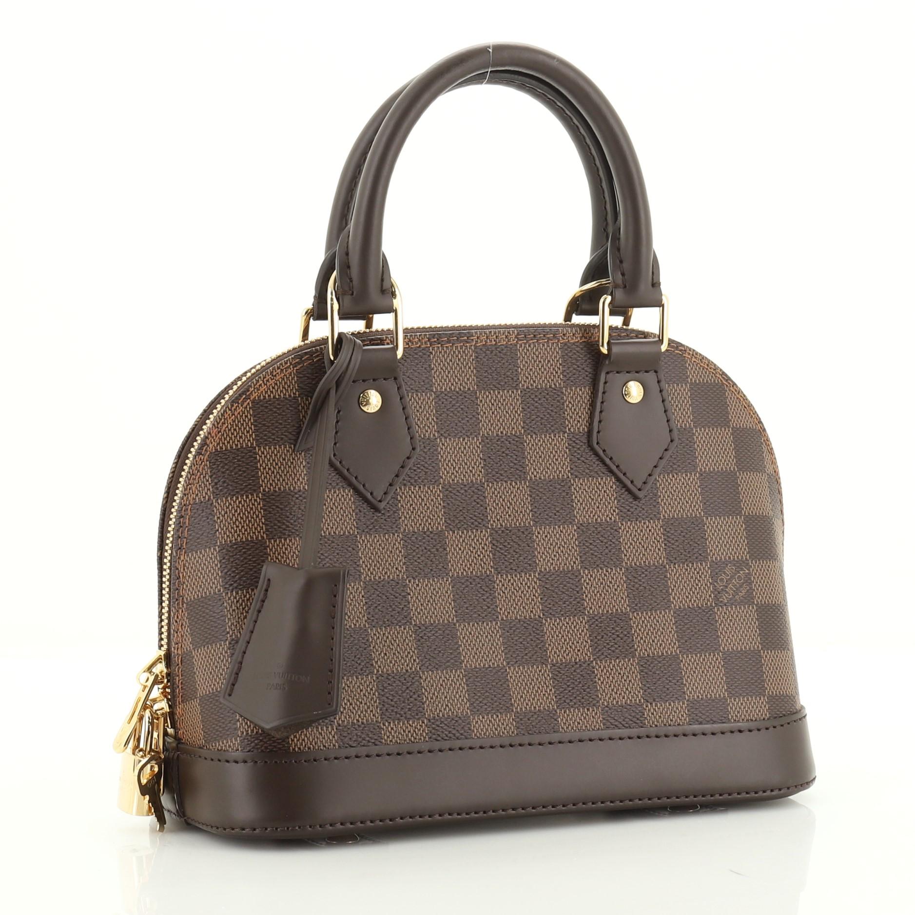 This Louis Vuitton Alma Handbag Damier BB, crafted from damier ebene coated canvas, features dual rolled handles, leather trim, and gold-tone hardware. Its two-way zip closure opens to a red fabric interior with slip pockets. Authenticity code